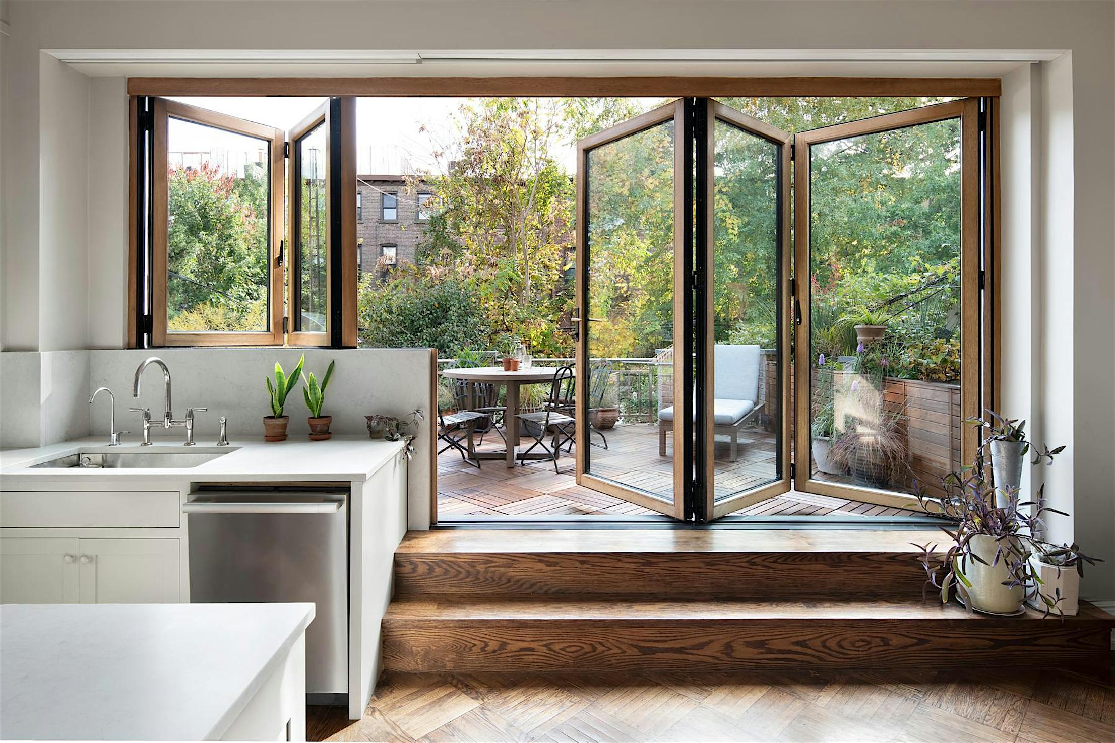 Modern home with partially open folding glass patio doors revealing indoor workspace, blending indoor and outdoor spaces