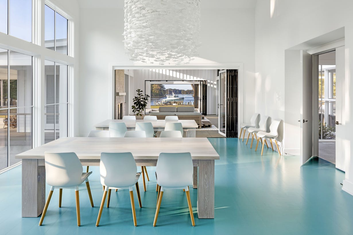 A dining room with blue floors, white chairs and folding glass walls overlooking the ocean