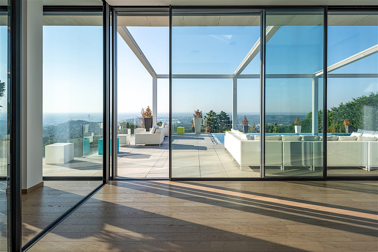 Large sliding glass doors open to a spacious patio with white outdoor furniture, offering a seamless transition to the scenic landscape under a clear blue sky.