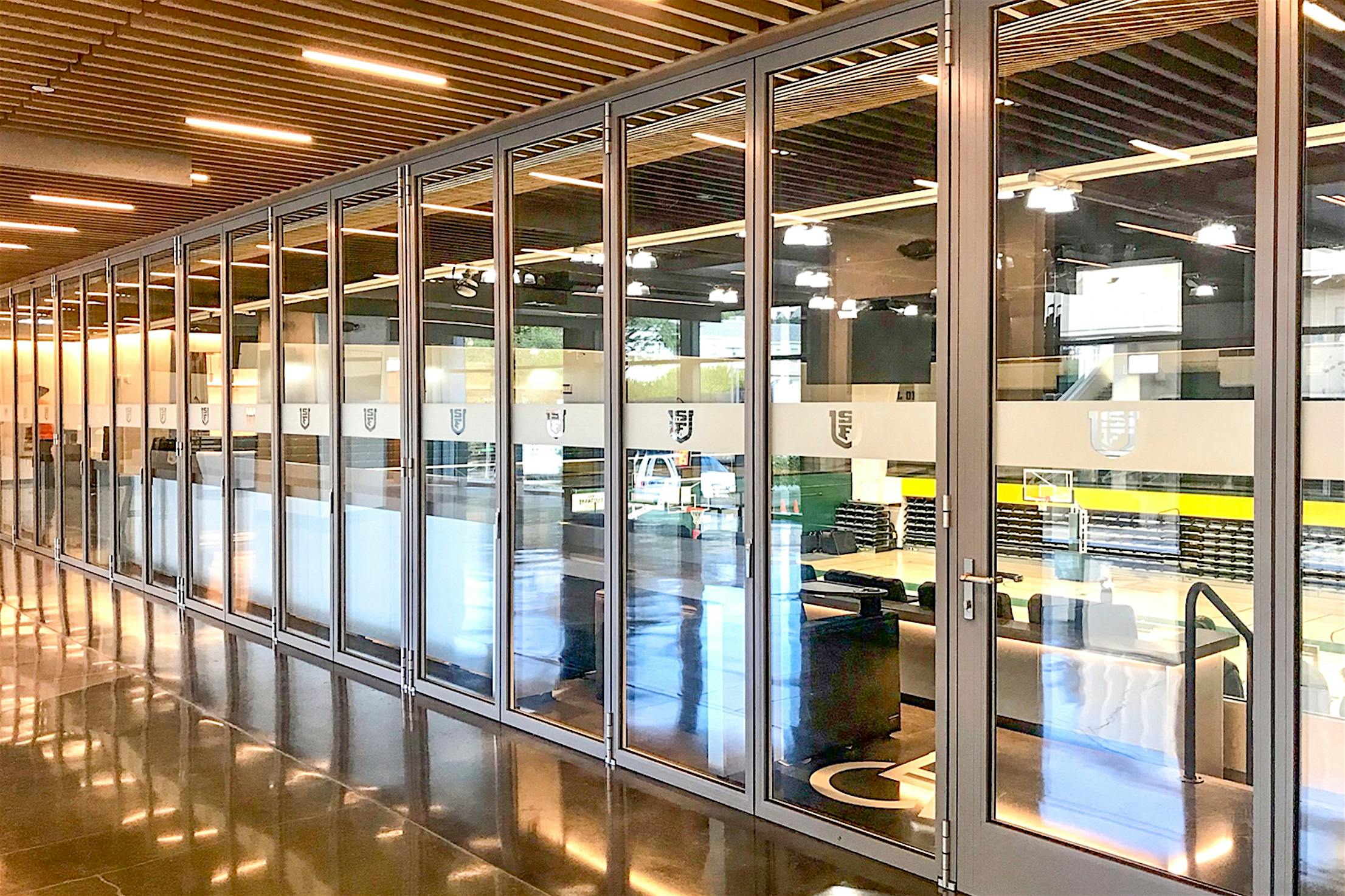 A modern basketball venue boasts a long acoustic glass walls with multiple vertical panels