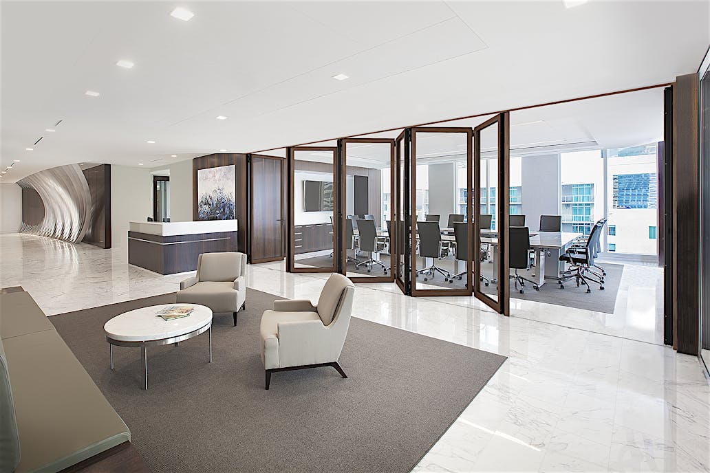 Modern office interior with a glass-partitioned conference room with a long table and chairs, enhanced by interior wood-framed folding glass doors for superior acoustical control.