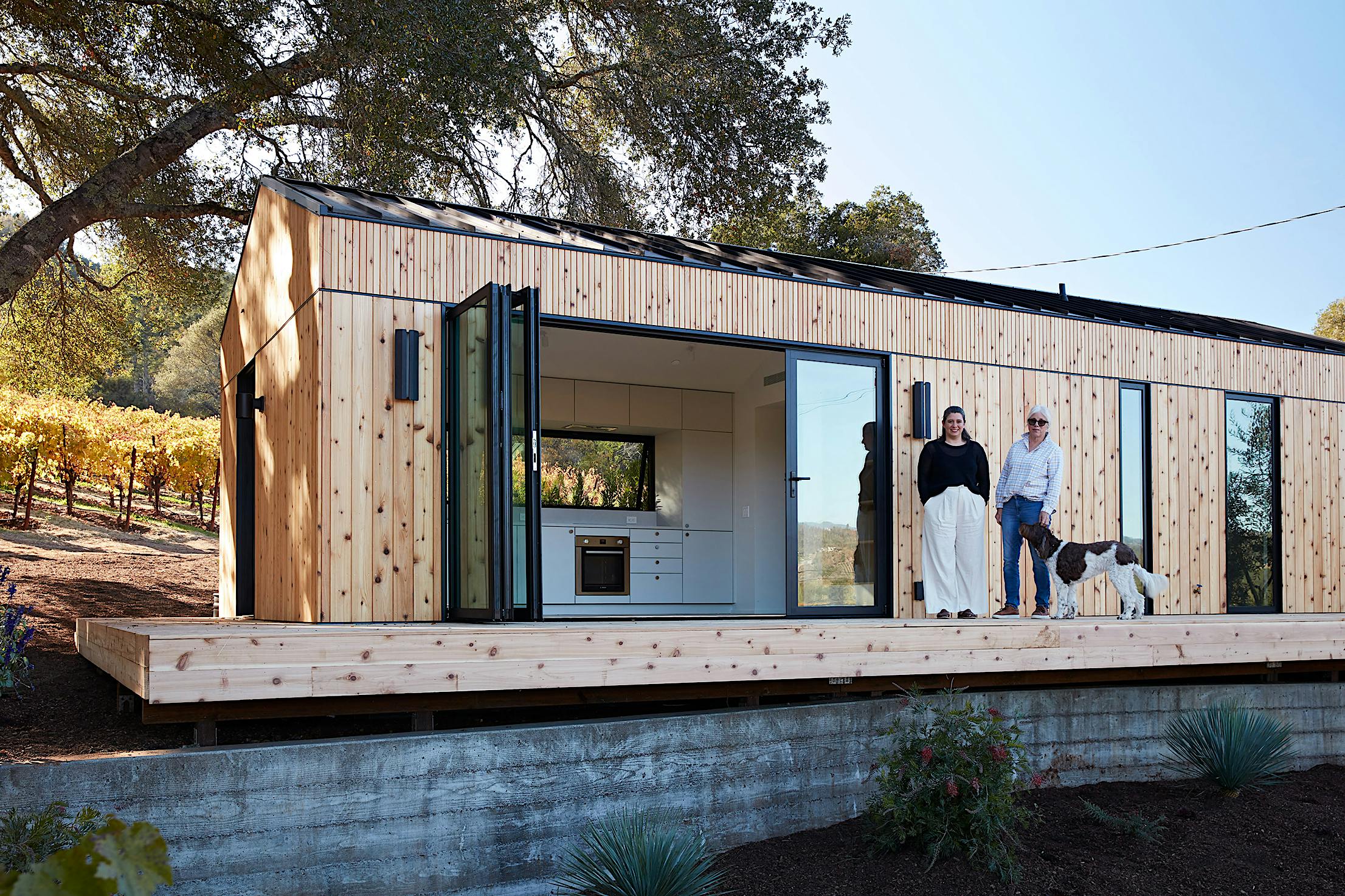 The Dwell House ADU - A modern wooden modular home with large folding glass doors..
