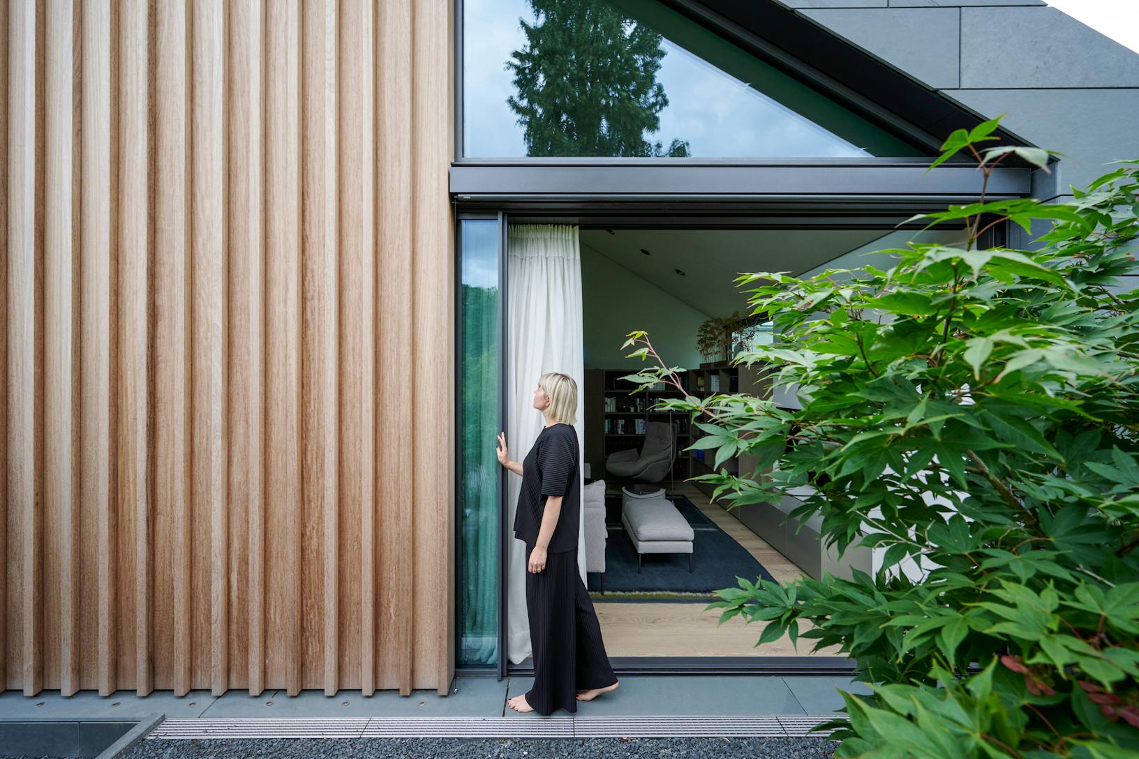 A woman is standing outside of a modern house with sliding glass walls