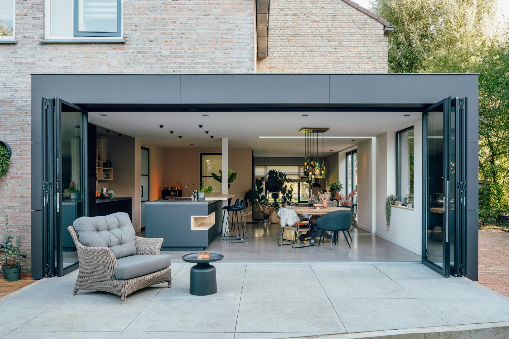 A modern patio with a black chair and table - open exterior folding glass walls