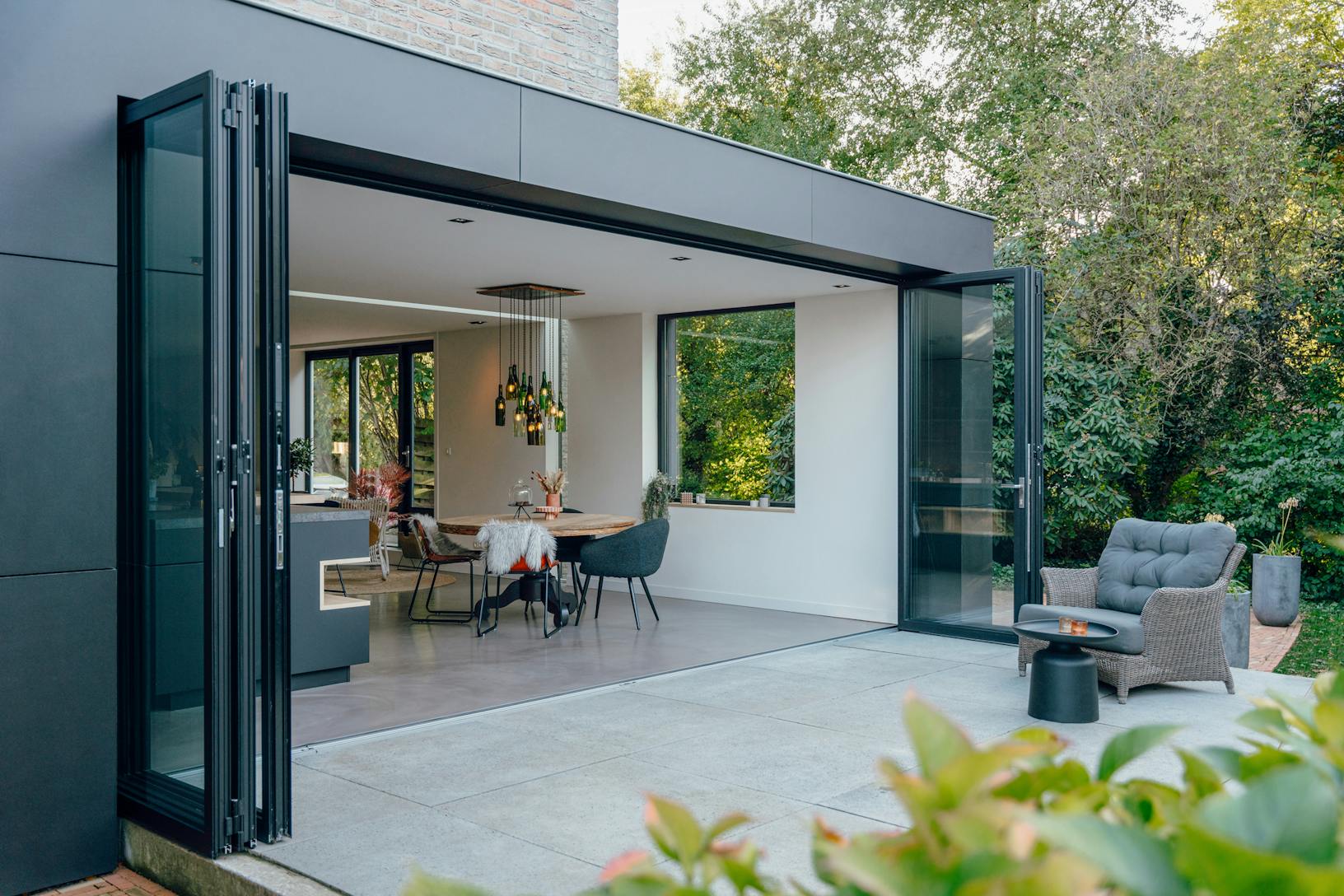 A modern patio with a black chair and table - open exterior folding doors