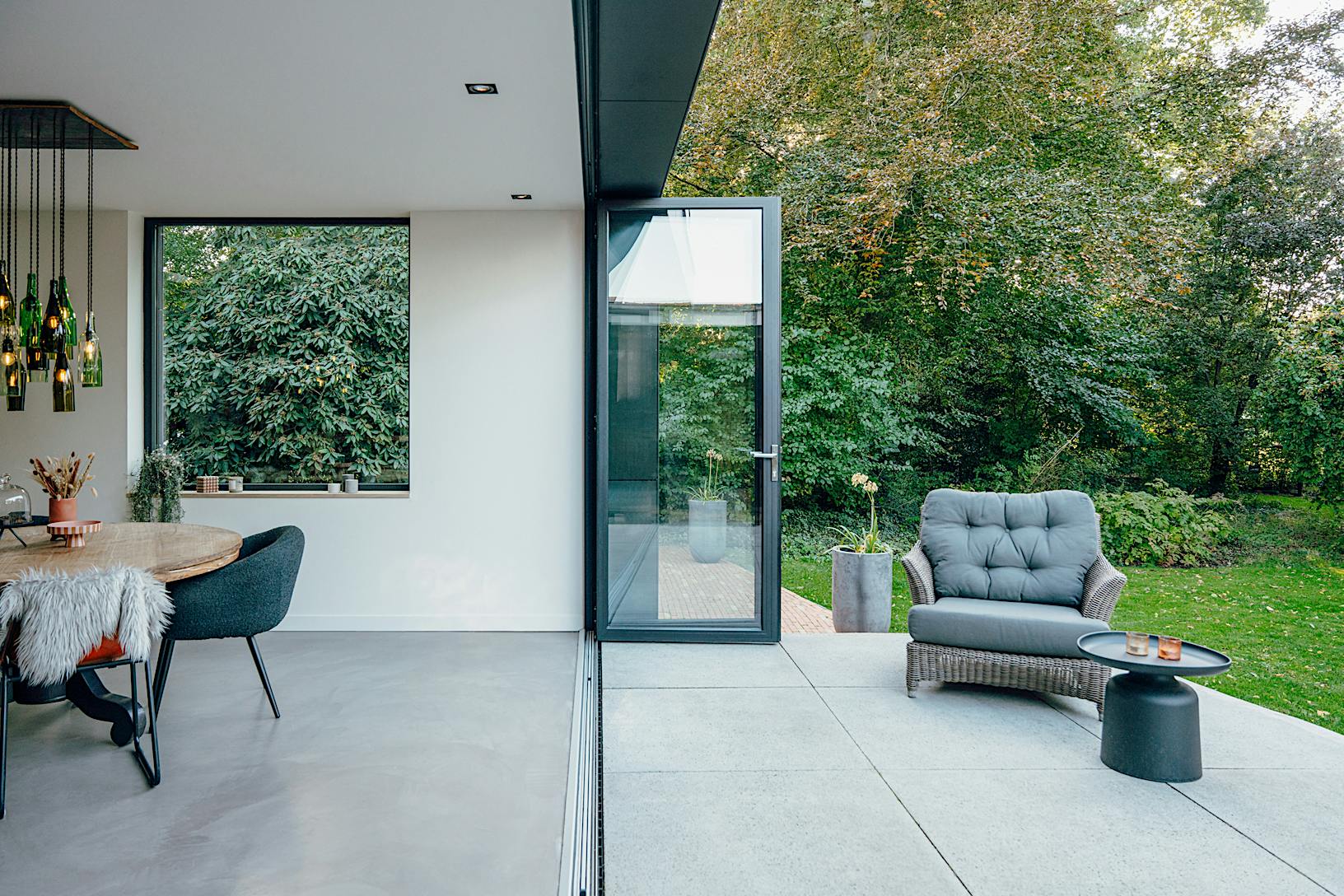 A modern patio with a black chair and table - large opening glass walls