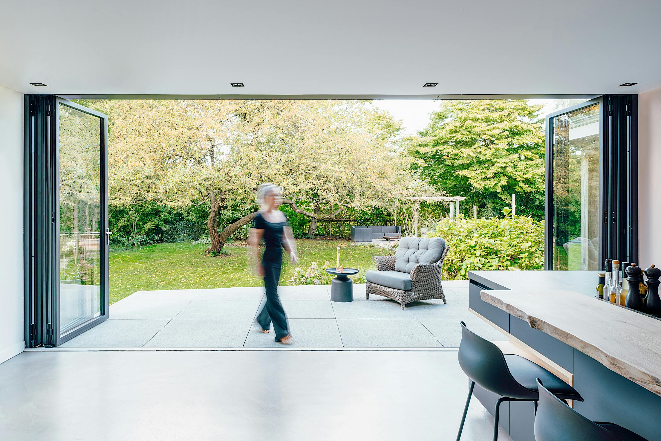 A woman walks through large folding patio doors into a kitchen