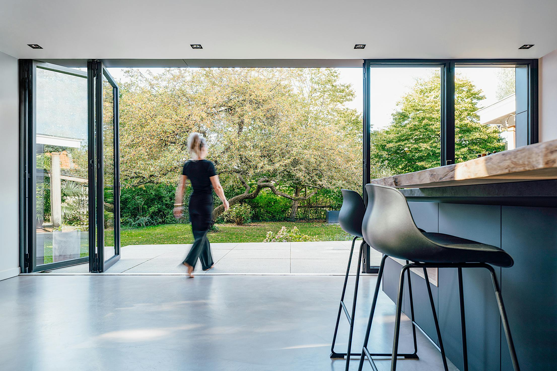 A woman walks through a glass accordion door into a kitchen