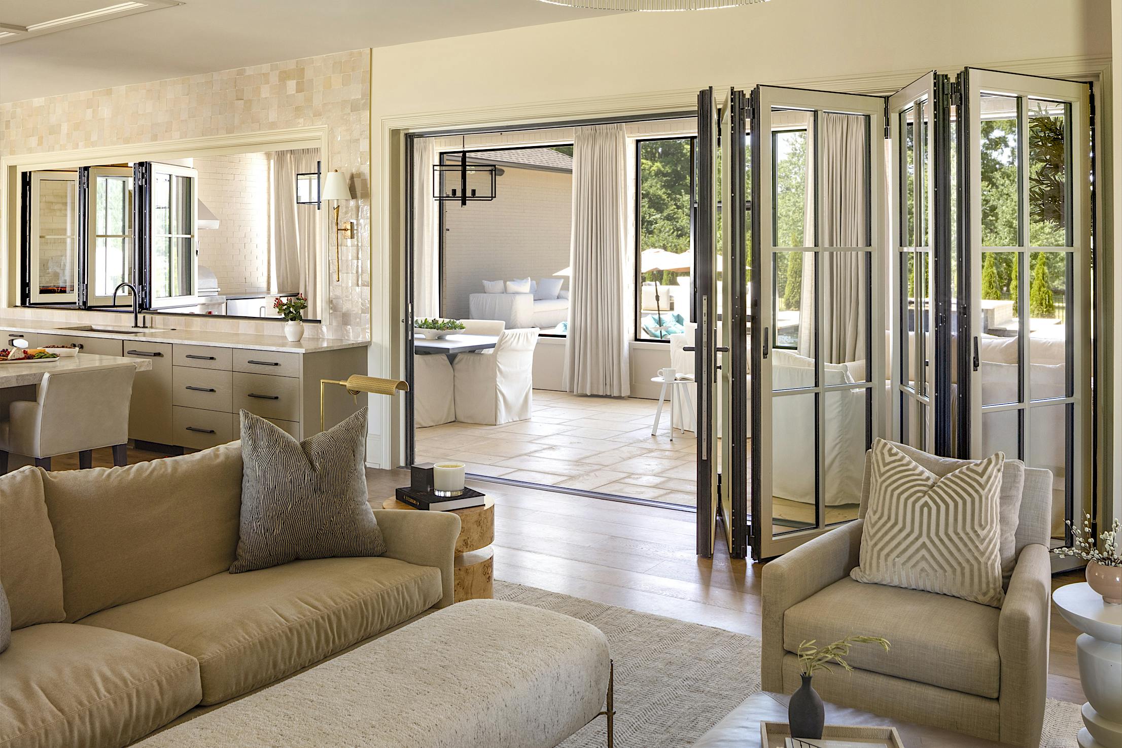 A beige couch in a living room with glass wall panels and kitchen windows