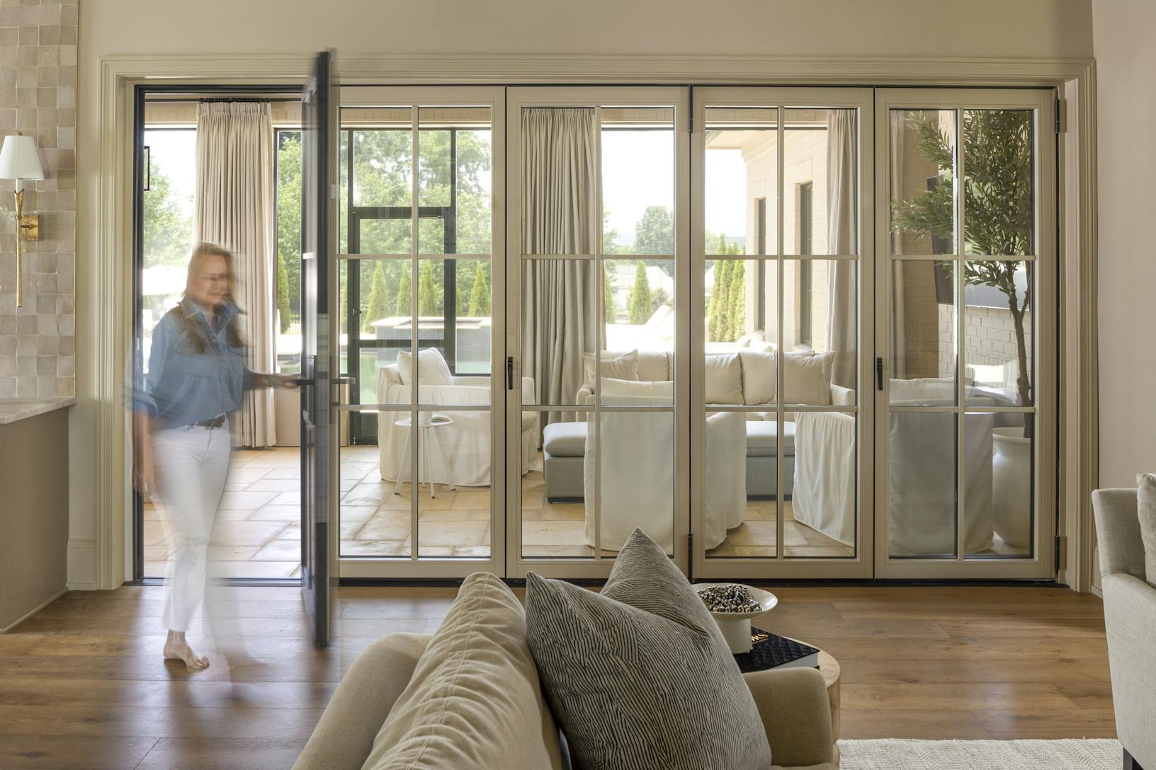 A woman standing in a living room with swing doors leading to the dining room and kitchen