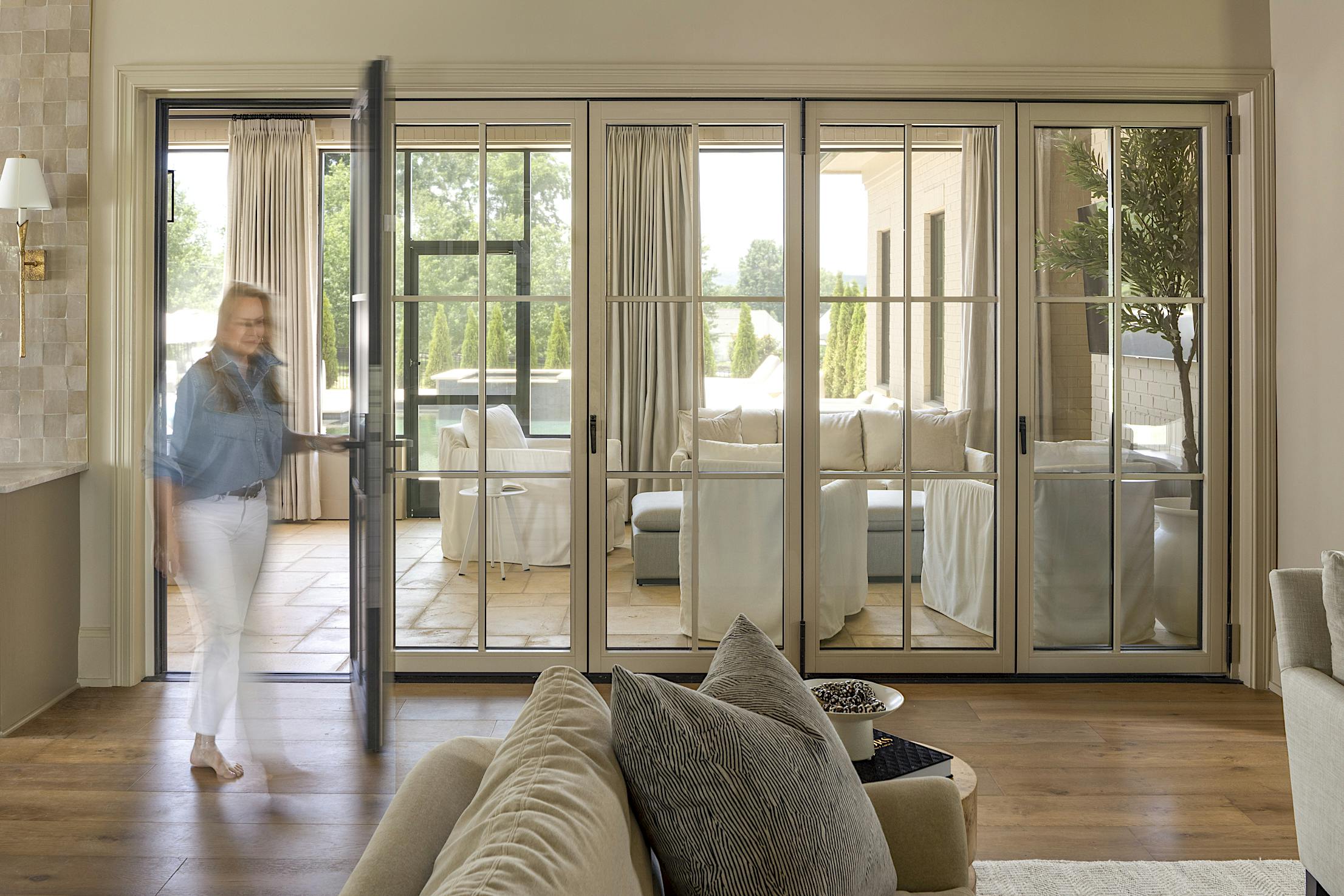 A woman standing in a living room with swing doors leading to the dining room and kitchen