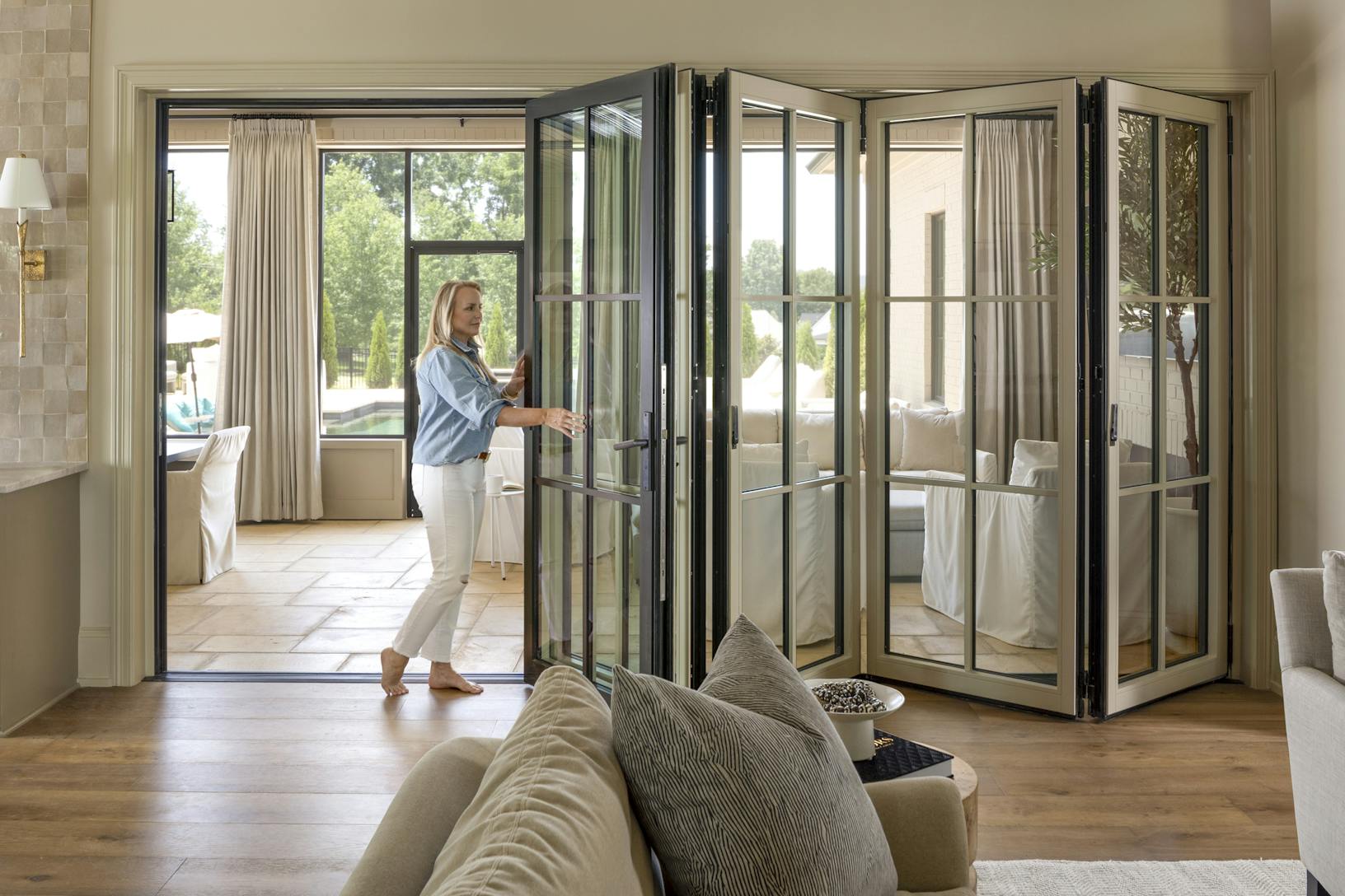 A woman opening a glass door in a living room with glass walls