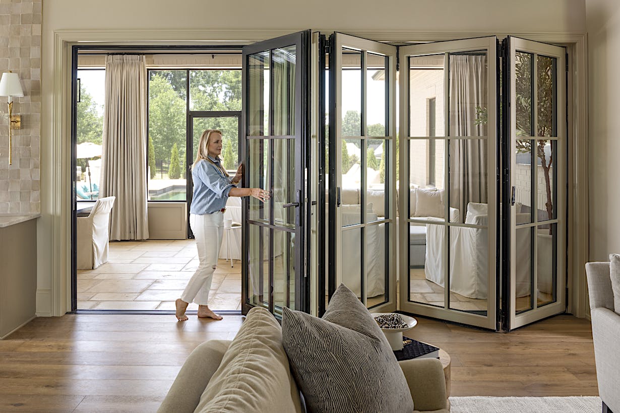 A woman opening a glass door in a living room with glass walls