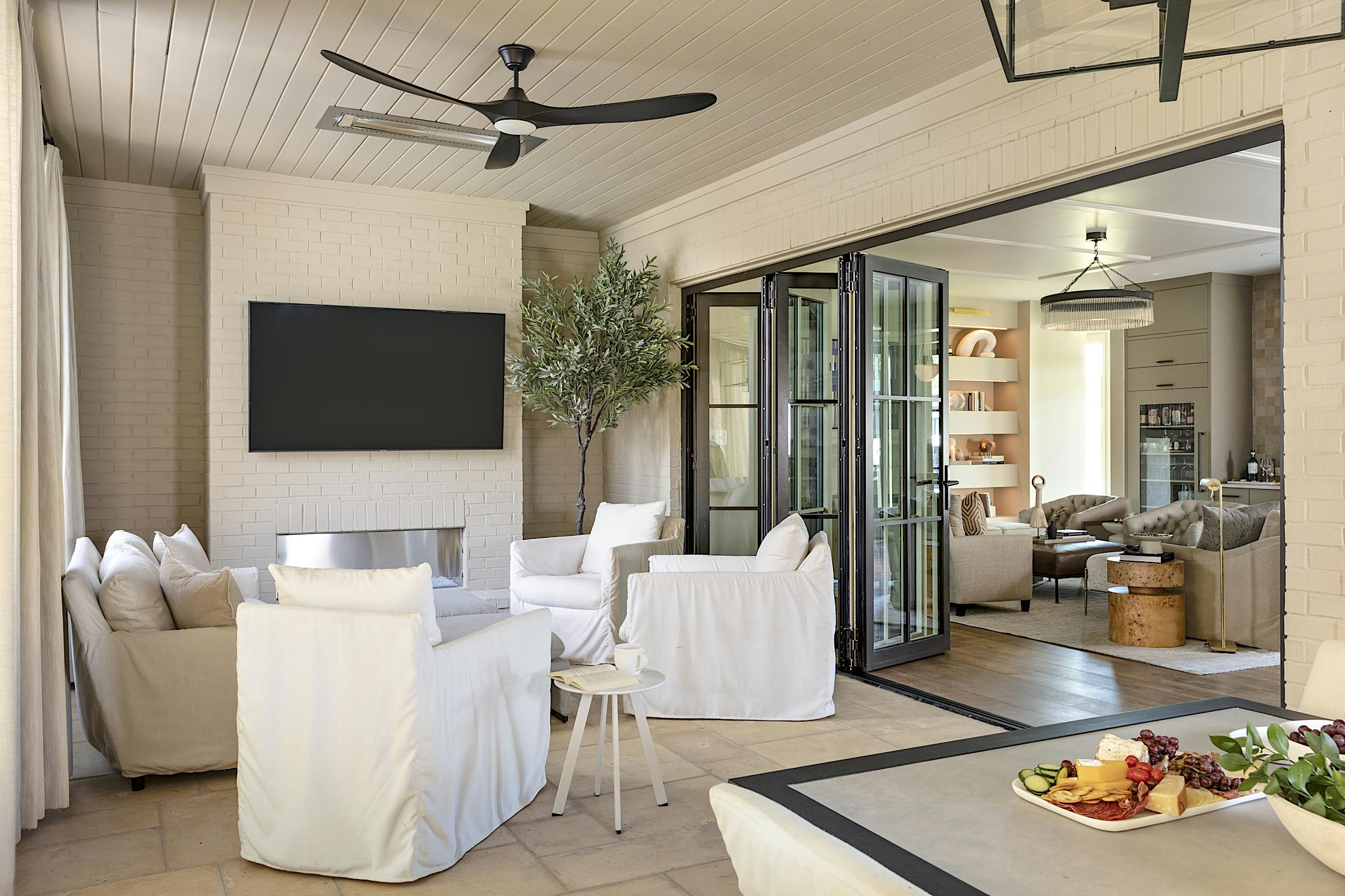 A living room with white furniture, folding glass walls