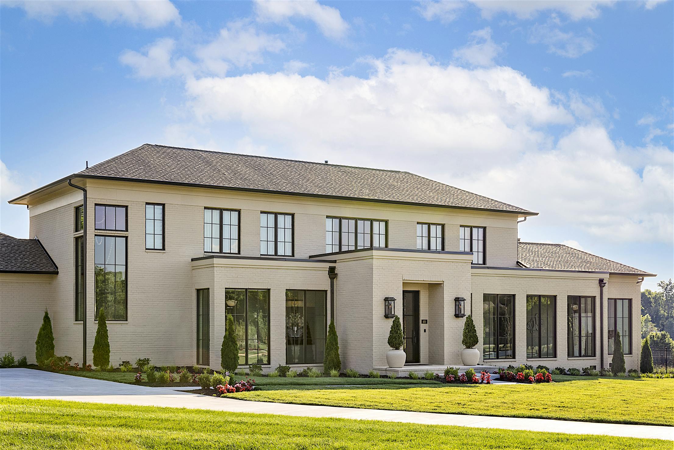 The exterior of a large house with glass wall panels offering views of the dining room and kitchen, surrounded by a spacious lawn