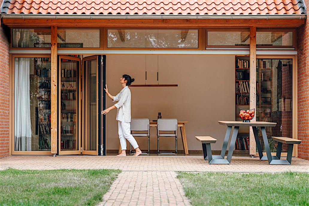 Wood-framed folding glass doors at Bramsche Farmhouse create unobstructed openings between indoor and outdoor areas