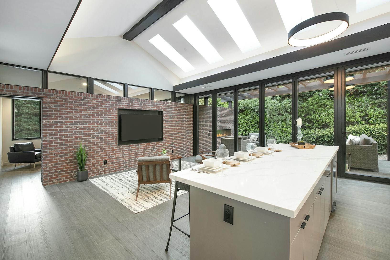 ADU modern kitchen with a brick wall and a TV, featuring an Aluminum Clad Folding Glass Wall for connecting to the outdoor patio area