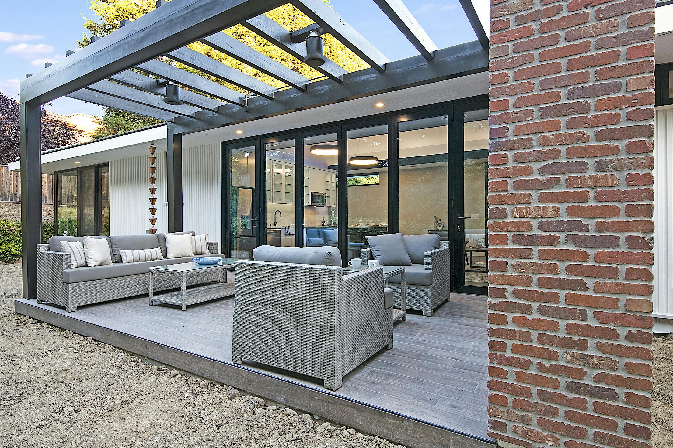 A modern patio with furniture and a brick wall featuring an Aluminum Clad Folding Glass Wall