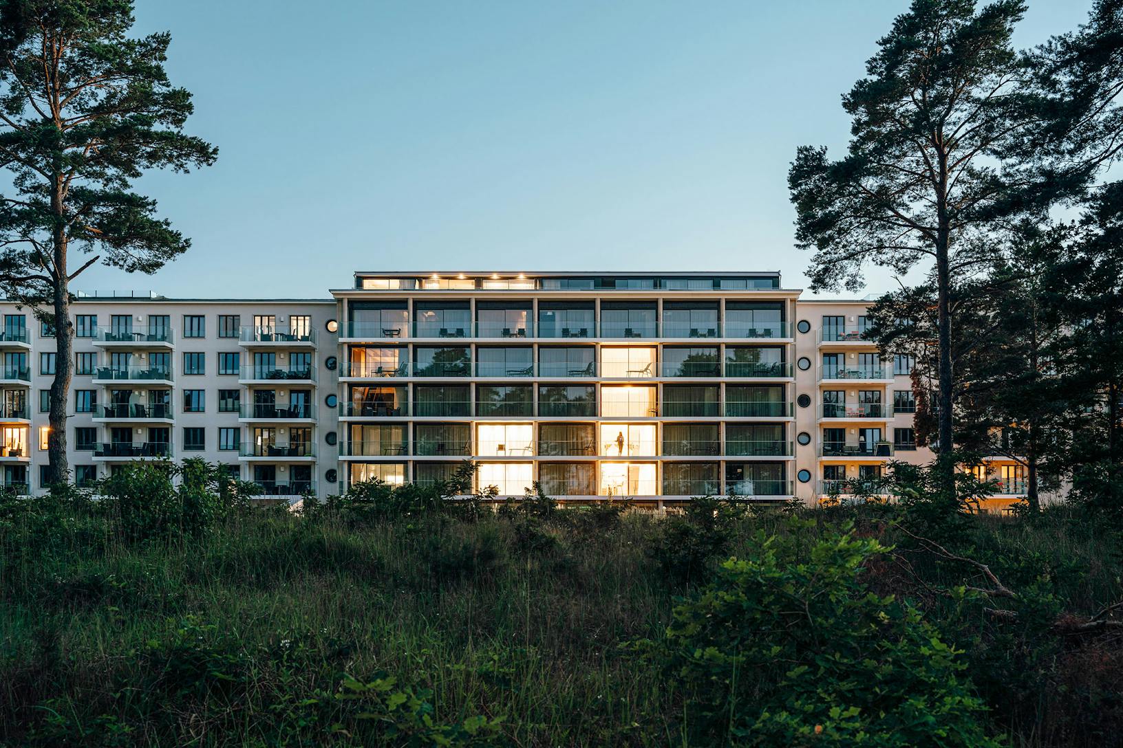 A multifamily apartment building with a sleek and modern architecture featuring minimal sliding glass walls, offering a breathtaking view of the dusk-lit forest