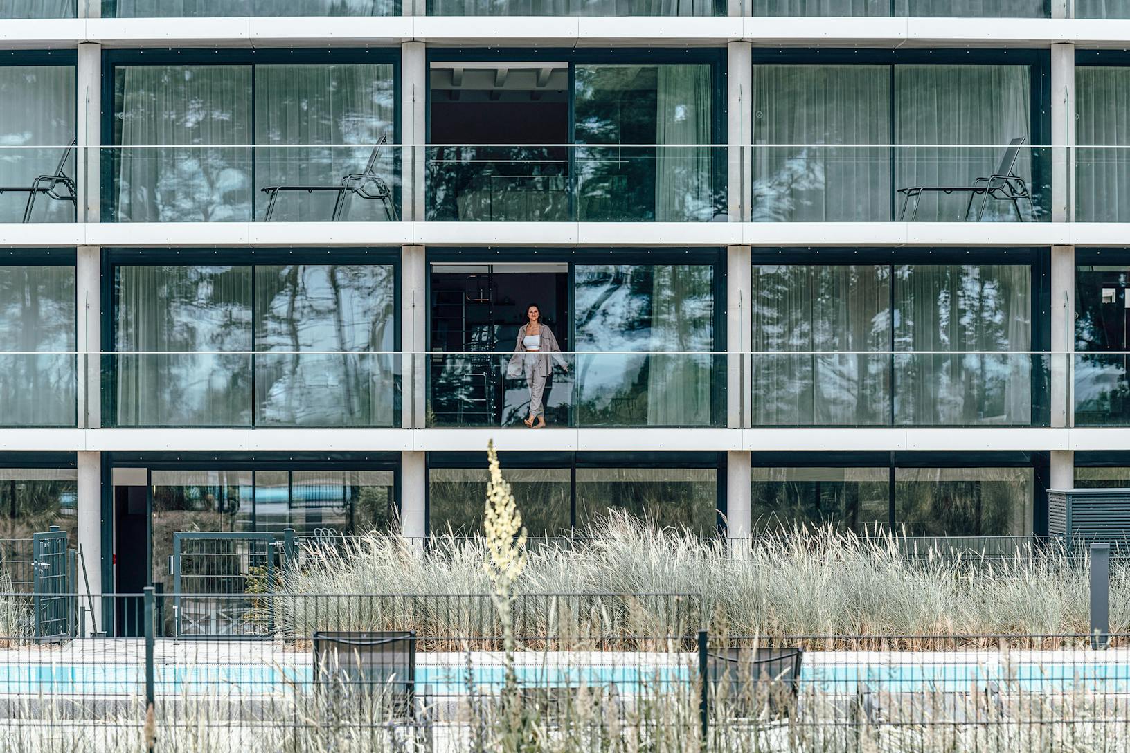 A woman enjoying the view from the glass-walled balcony of a multifamily apartment building