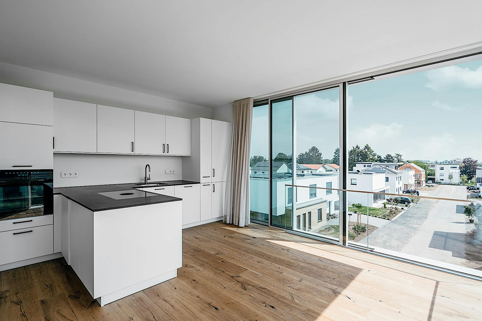 A modern kitchen with a large window overlooking a city, featuring minimal sliding glass walls perfect for condos