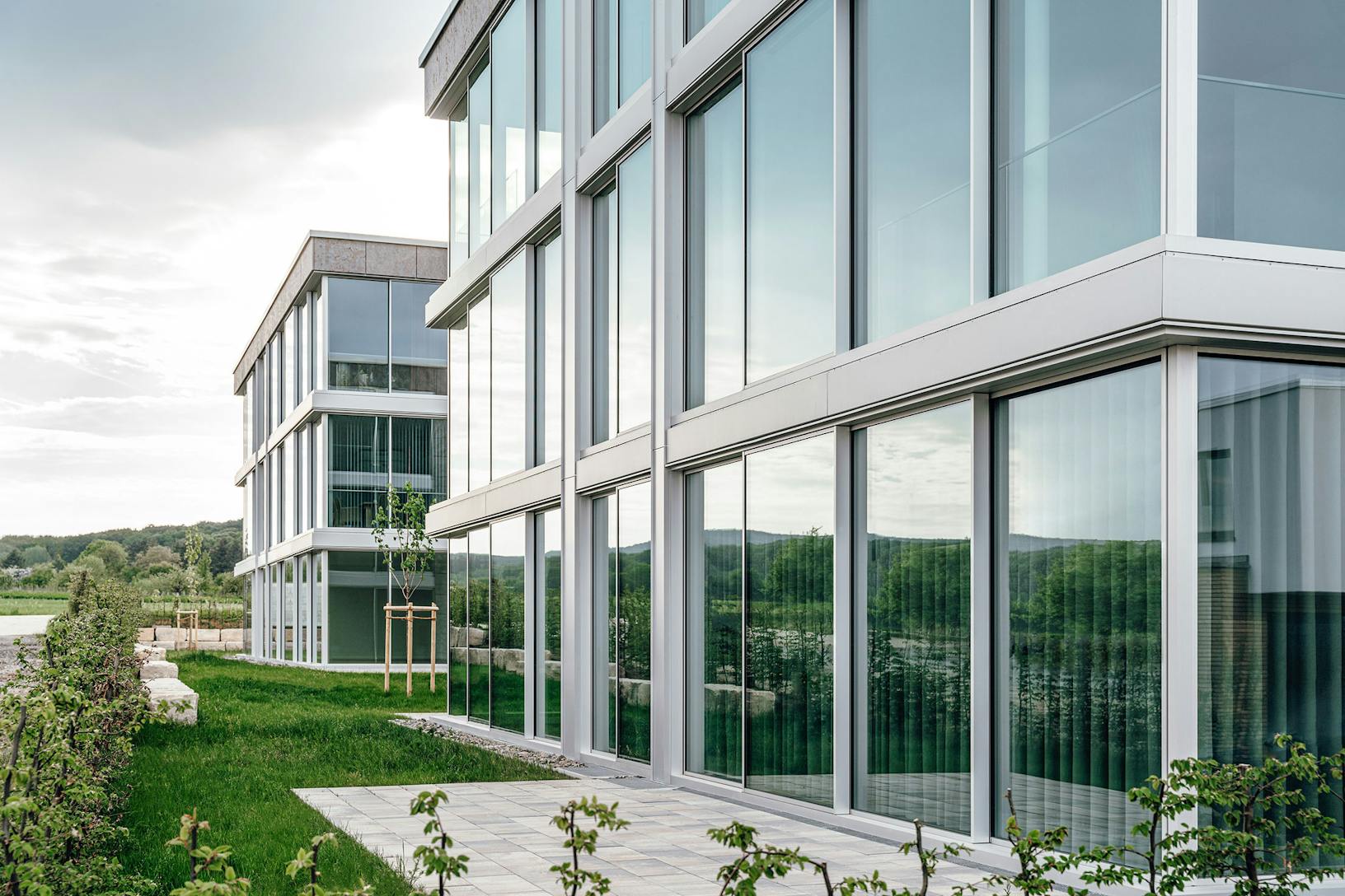 A modern condo building with minimal sliding glass walls, surrounded by a grassy area.