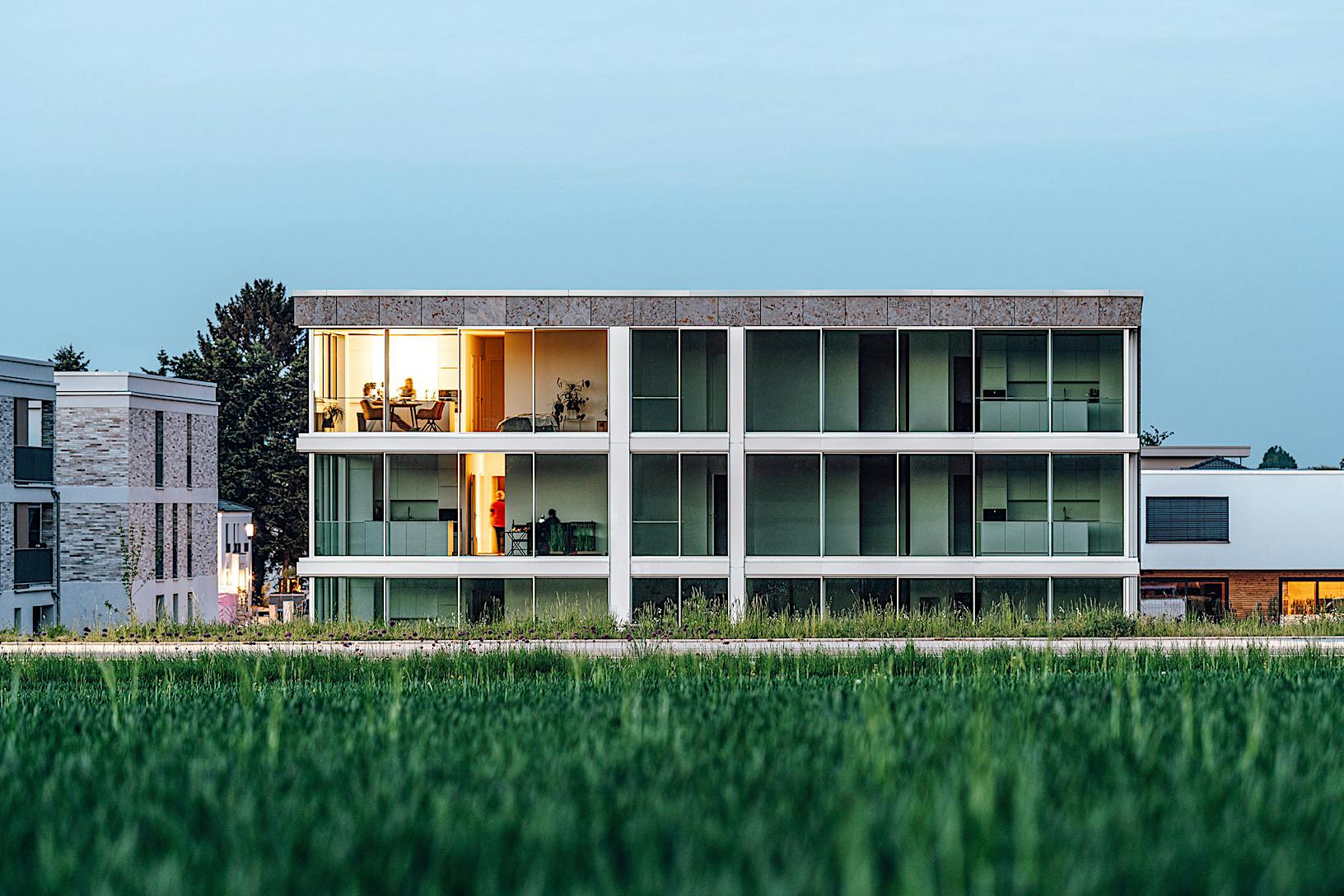 A modern multifamily building with glass walls, nestled in the middle of a serene grassy field