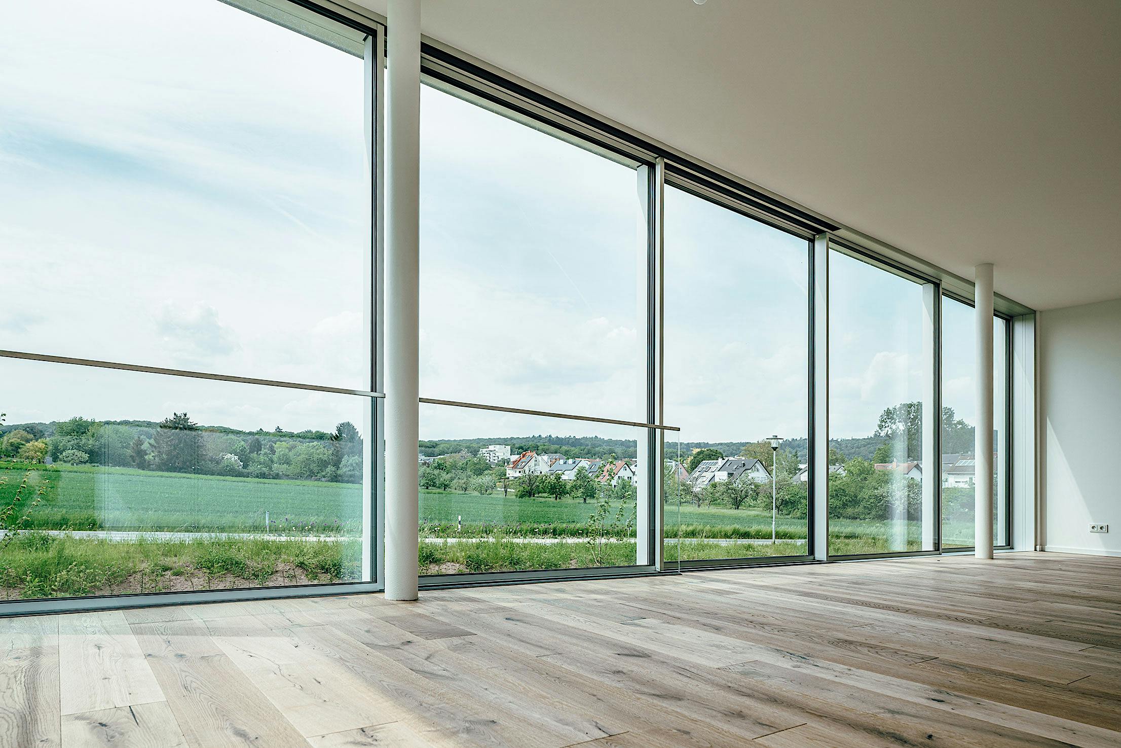An empty room with large windows and wood floors showcasing minimal sliding glass walls