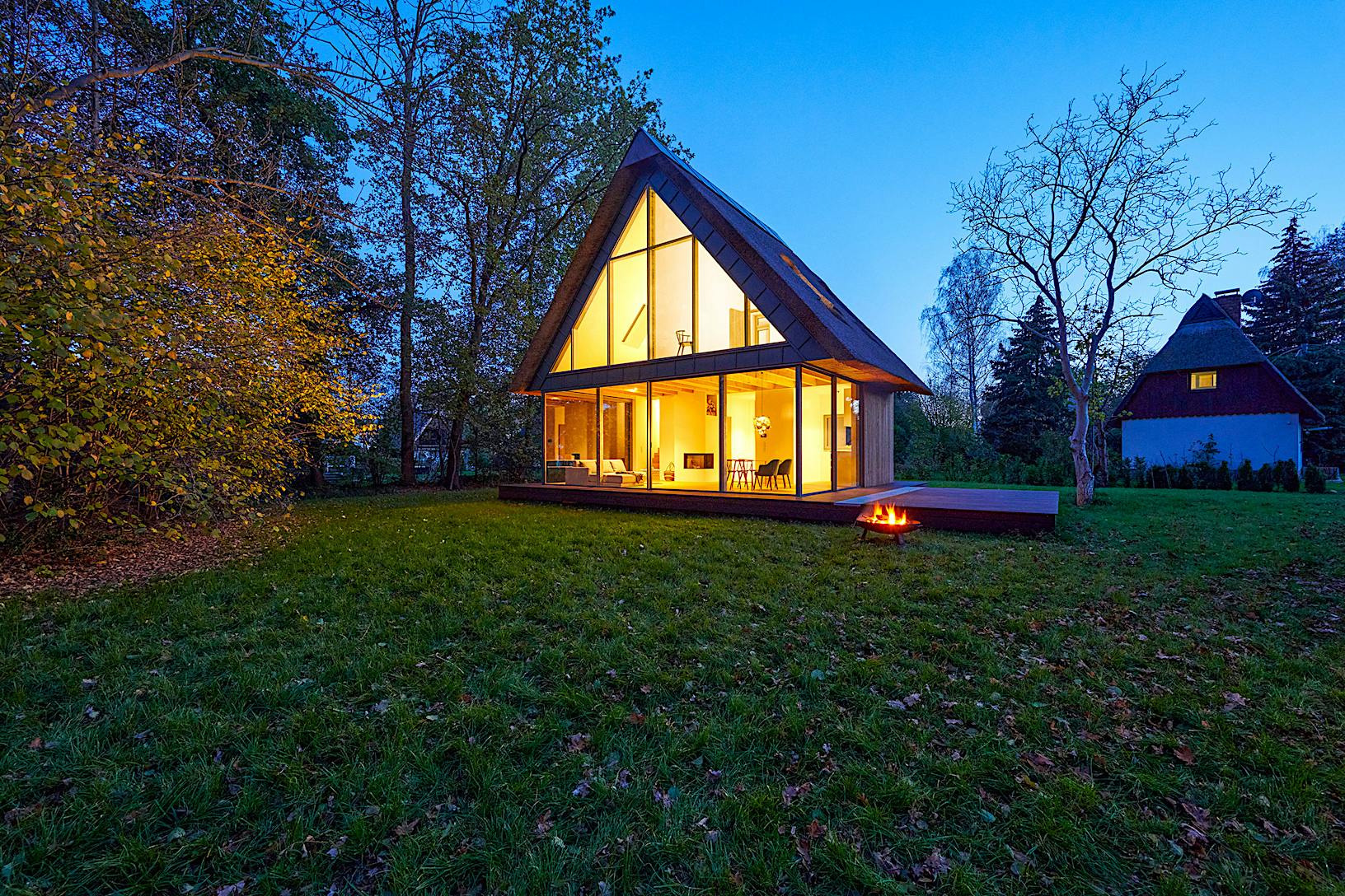 A modern cabin with minimal sliding glass walls in the woods at dusk