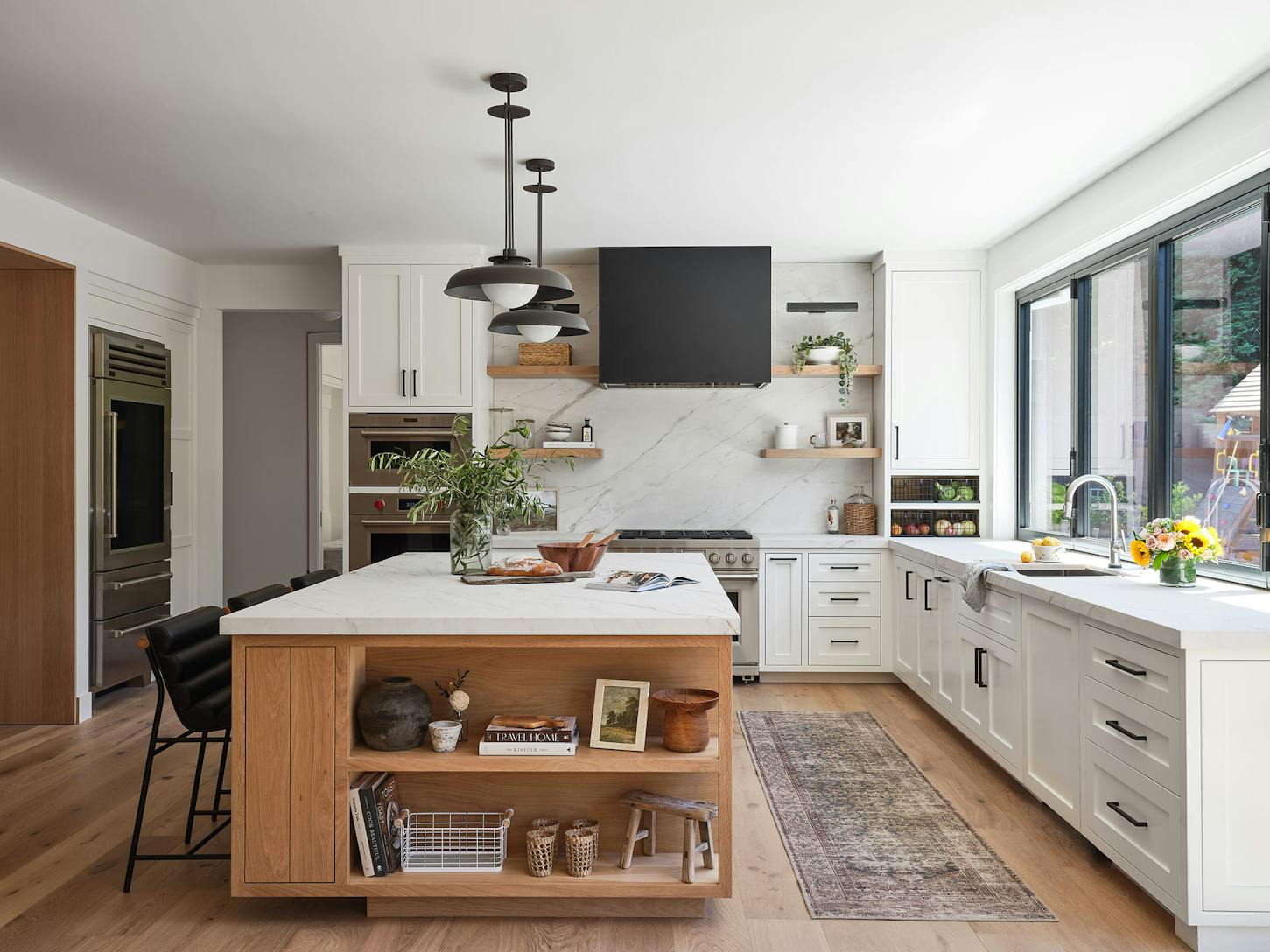 A modern kitchen with wood floors, a center island, and a window/door combination designed for a modern indoor outdoor kitchen
