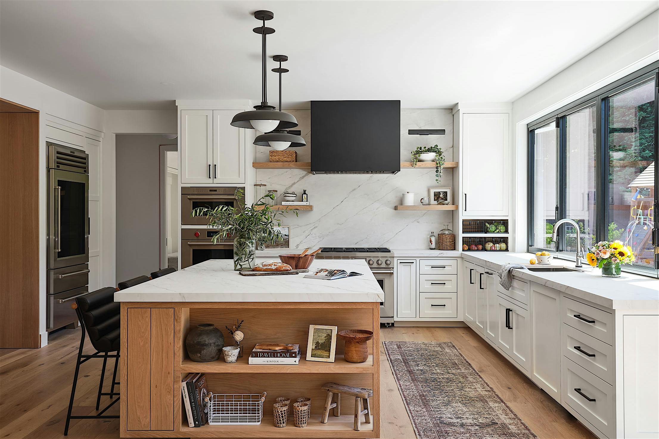 A modern kitchen with wood floors, a center island, and a window/door combination designed for a modern indoor outdoor kitchen