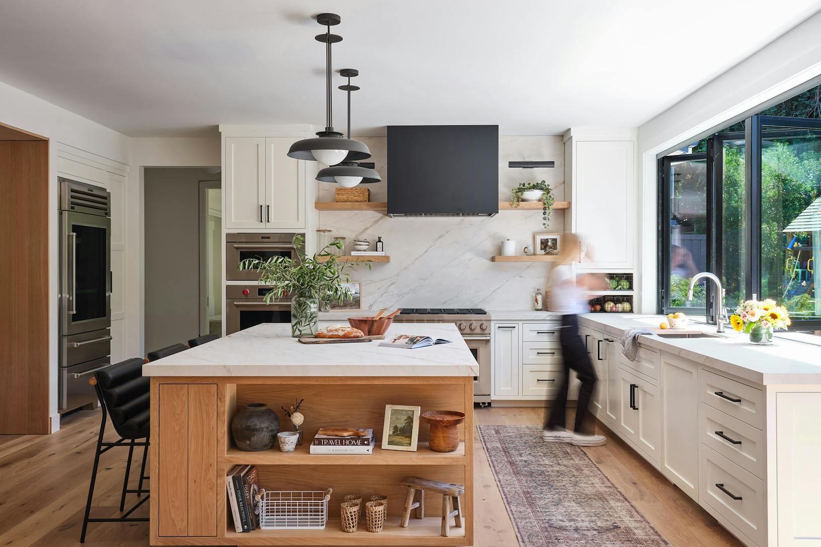 A modern kitchen with a center island, and a window/door combination designed for indoor outdoor open space