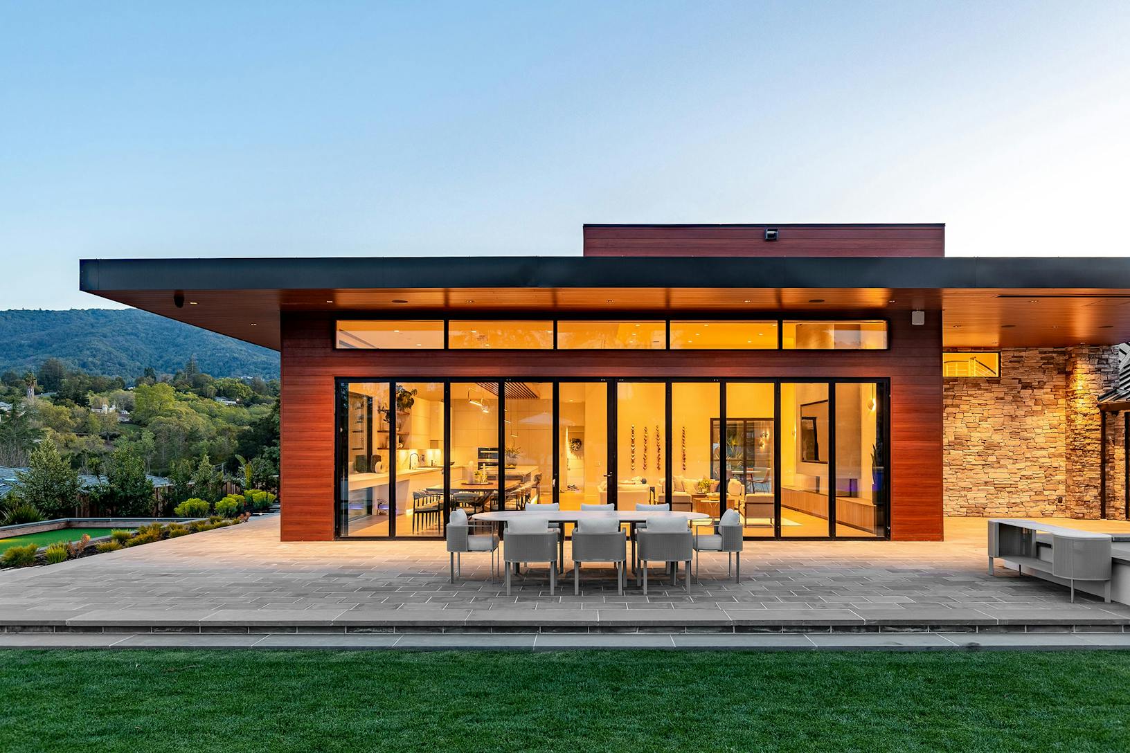 A modern home with bifold glass walls, offering a seamless connection to the large patio and outdoor dining area