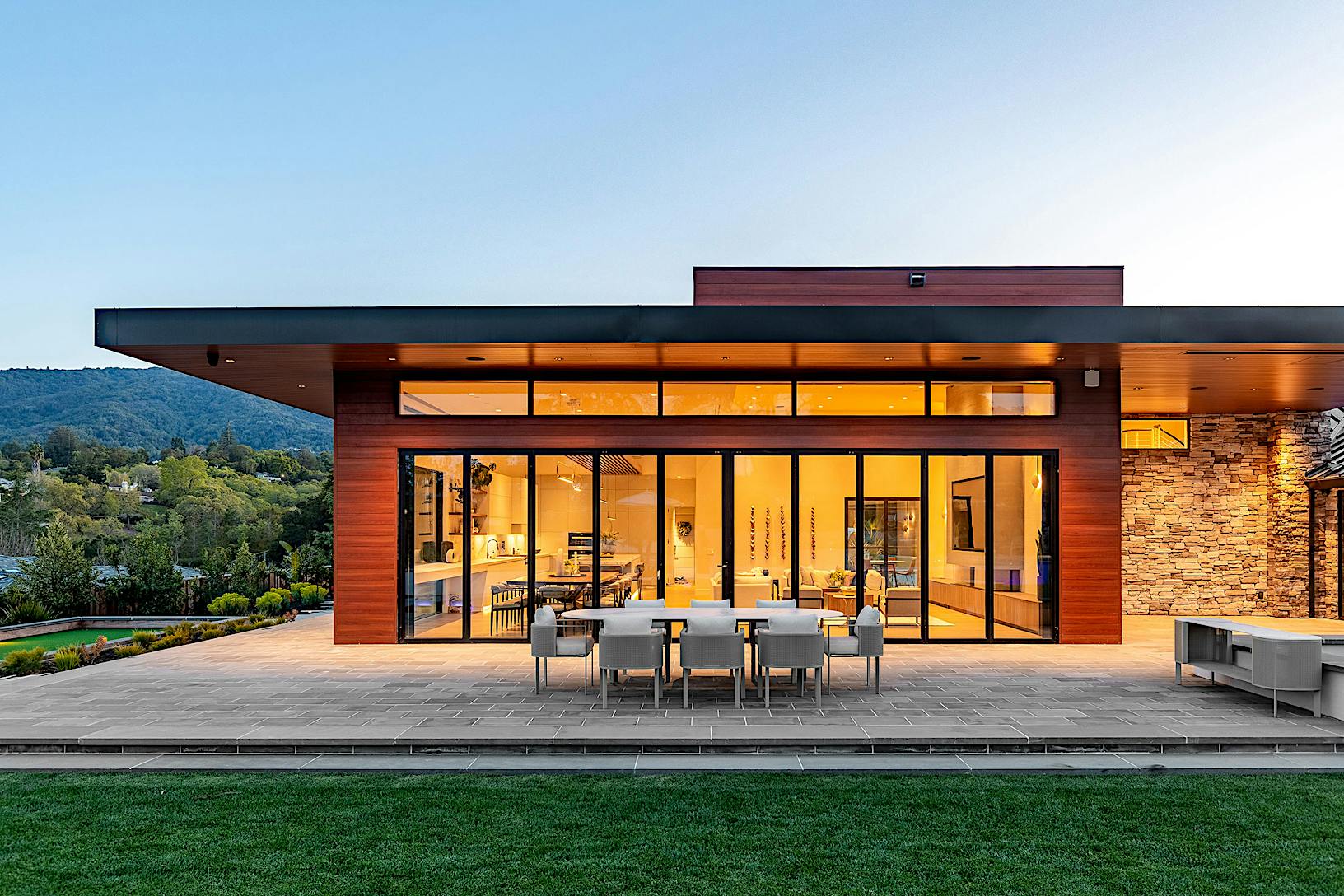 A modern home with bifold glass walls, offering a seamless connection to the large patio and outdoor dining area