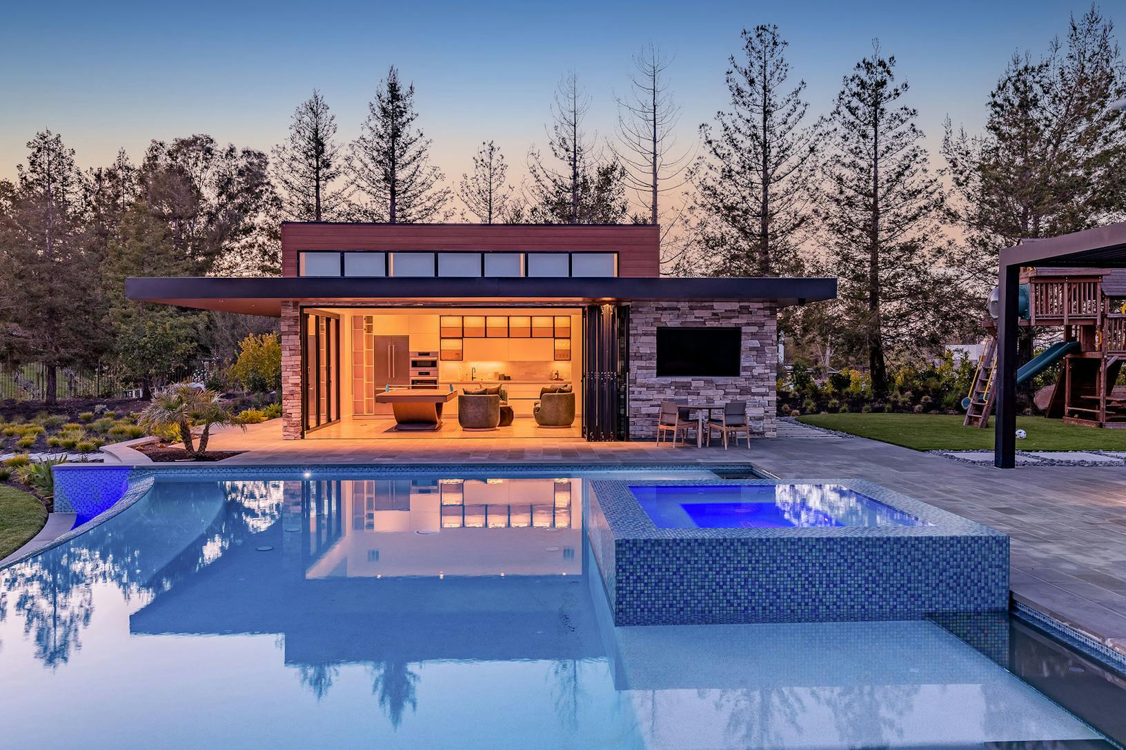 A modern pool house with bifold glass walls and a patio