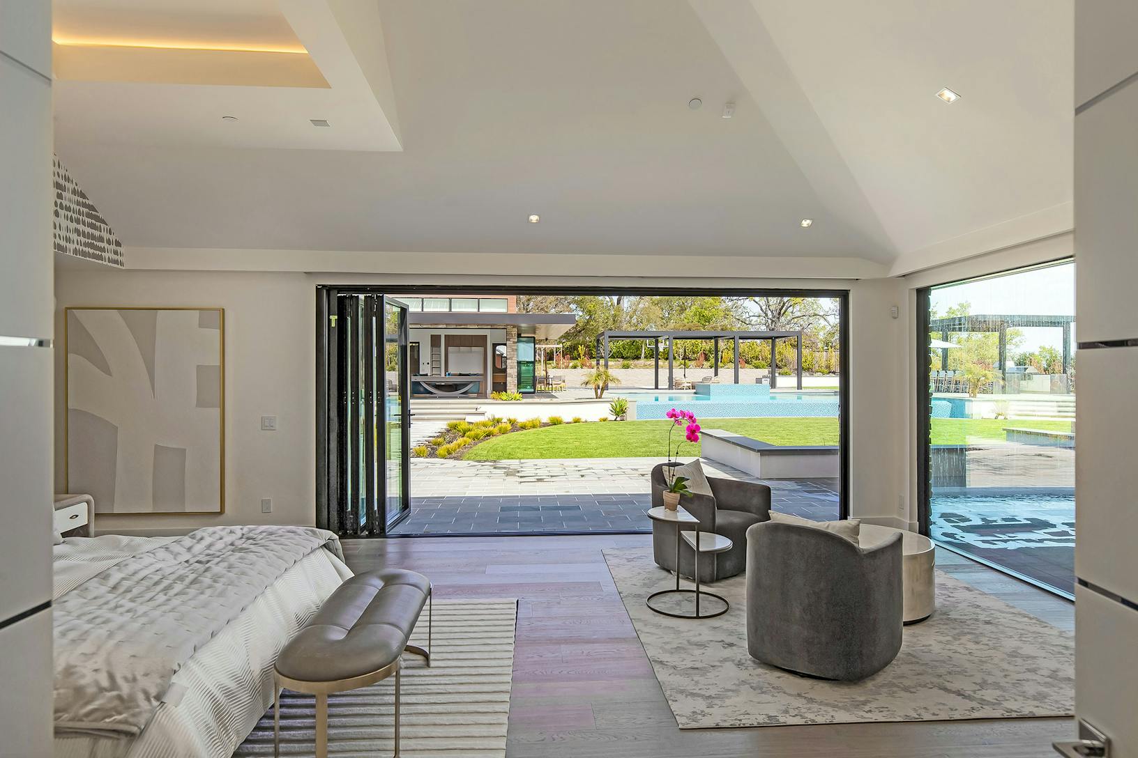 A bedroom with bifold glass walls leading to a pool