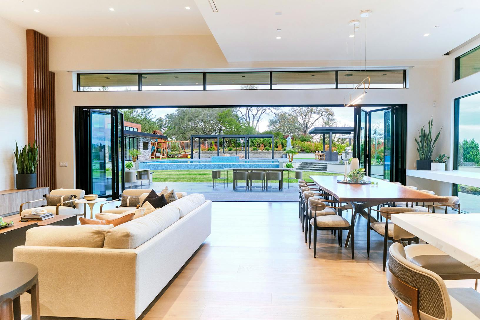 A contemporary living room featuring aluminum framed bifold glass walls, creating an indoor/outdoor area