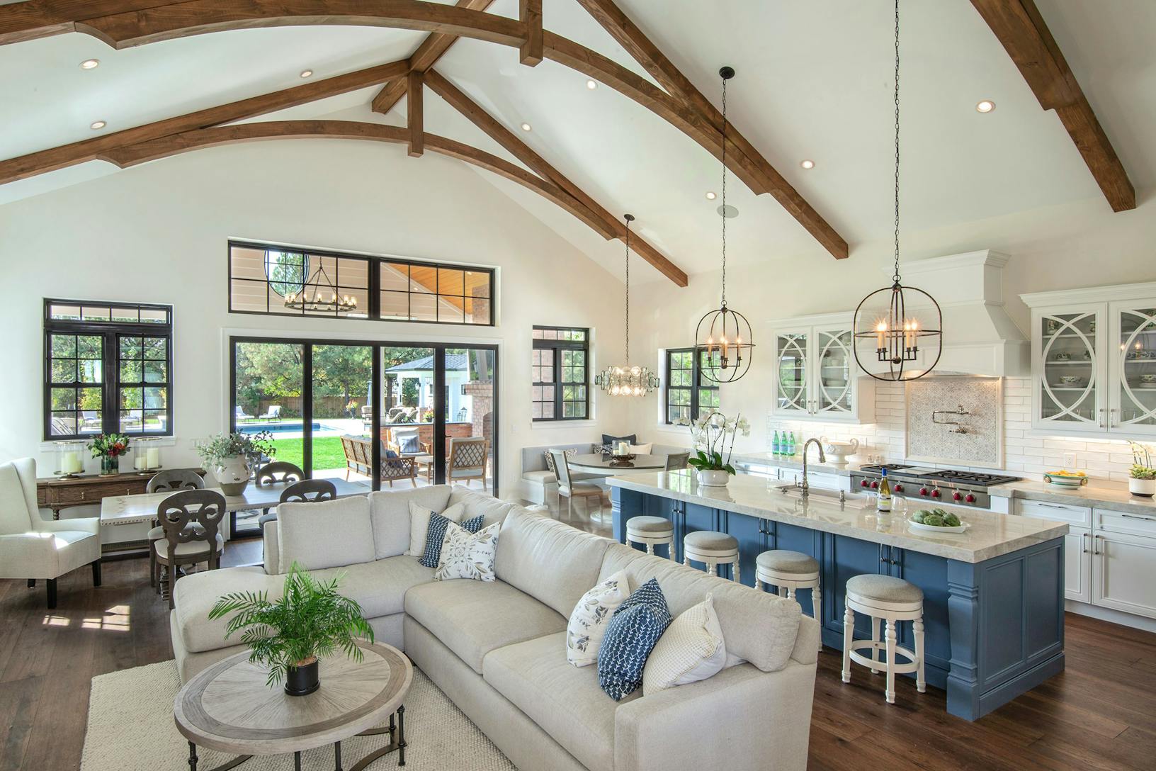 A large open kitchen and living room with folding glass walls, wood beams