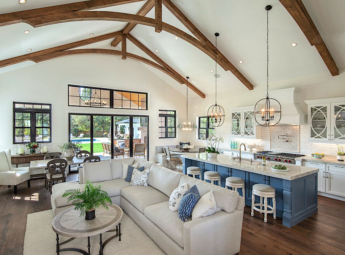 A large open kitchen and living room with folding glass walls, wood beams