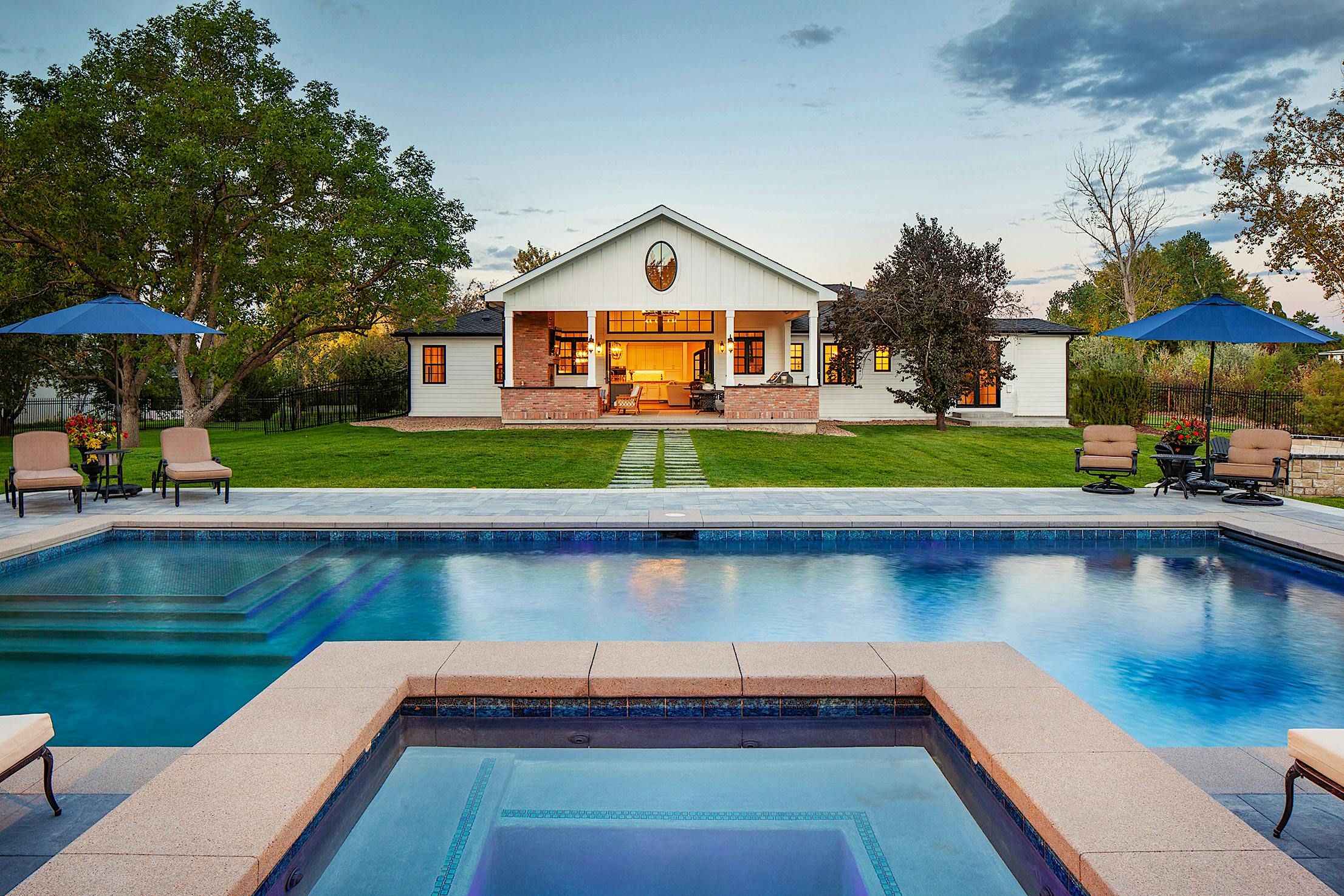 A swimming pool in front of a house with folding glass doors