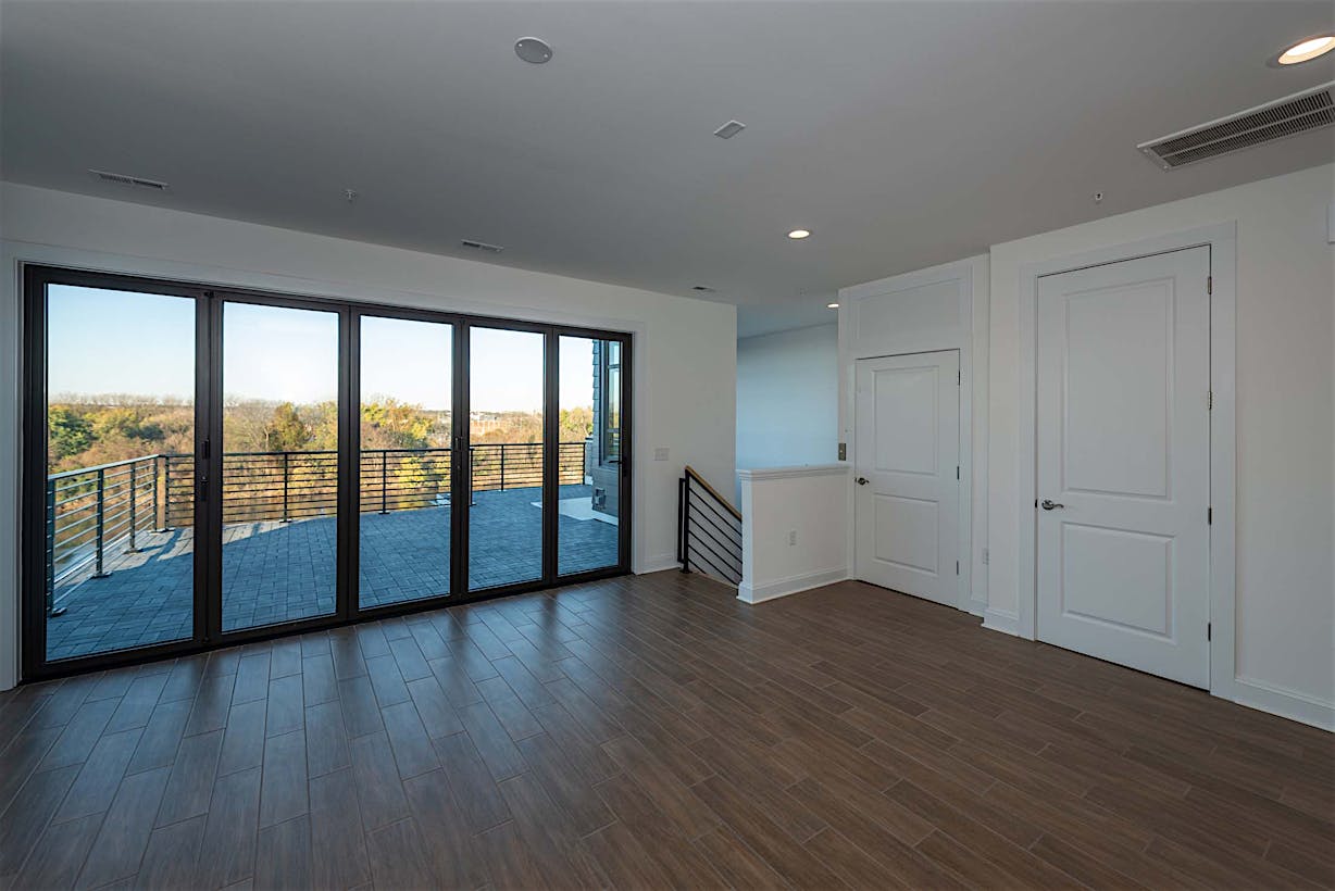 A modern room with wooden flooring, large folding glass doors opening to a balcony.