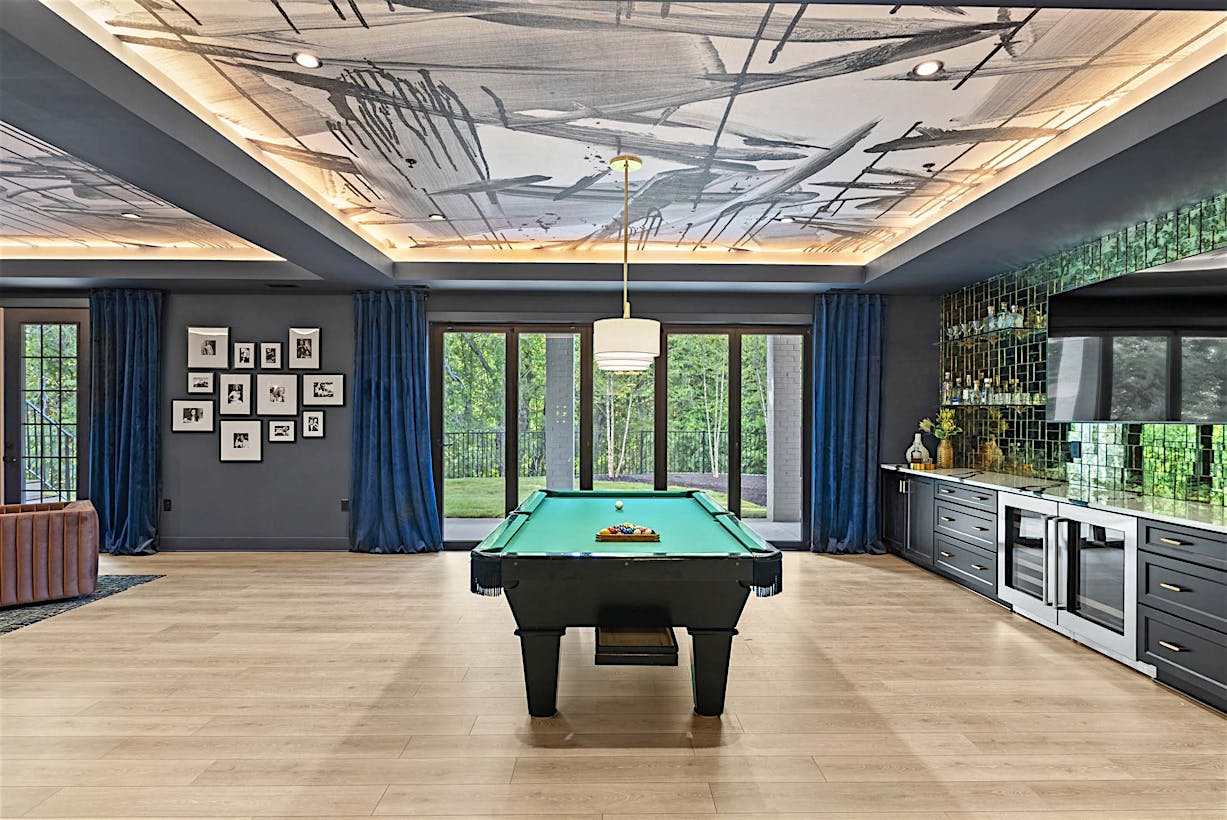 A modern game room with a pool table, black cabinetry, and floor-to-ceiling folding glass doors.