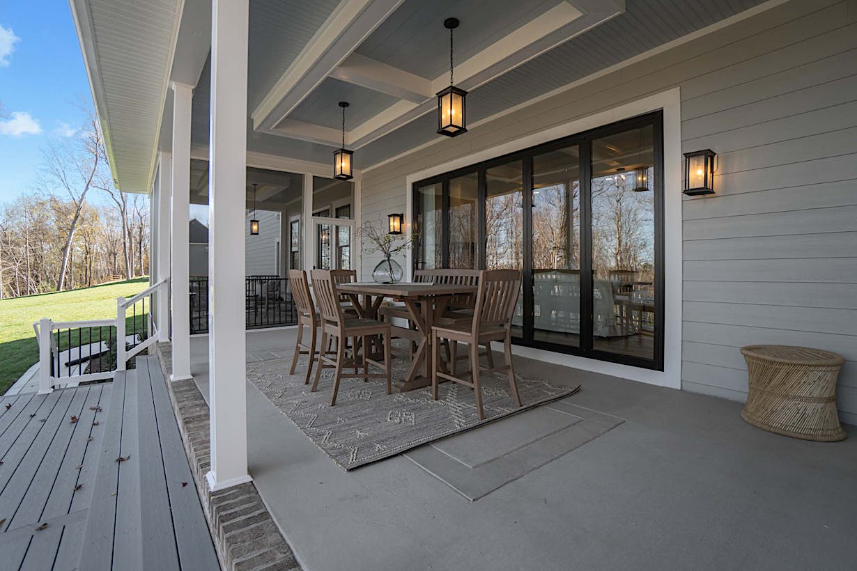A covered patio with a wooden dining set, hanging lantern lights, and folding patio doors that lead to the interior.