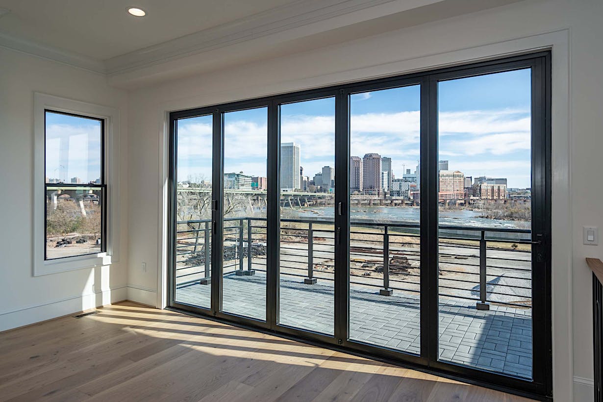 View of a city skyline and river through large glass doors in a modern room with hardwood floors and white walls.
