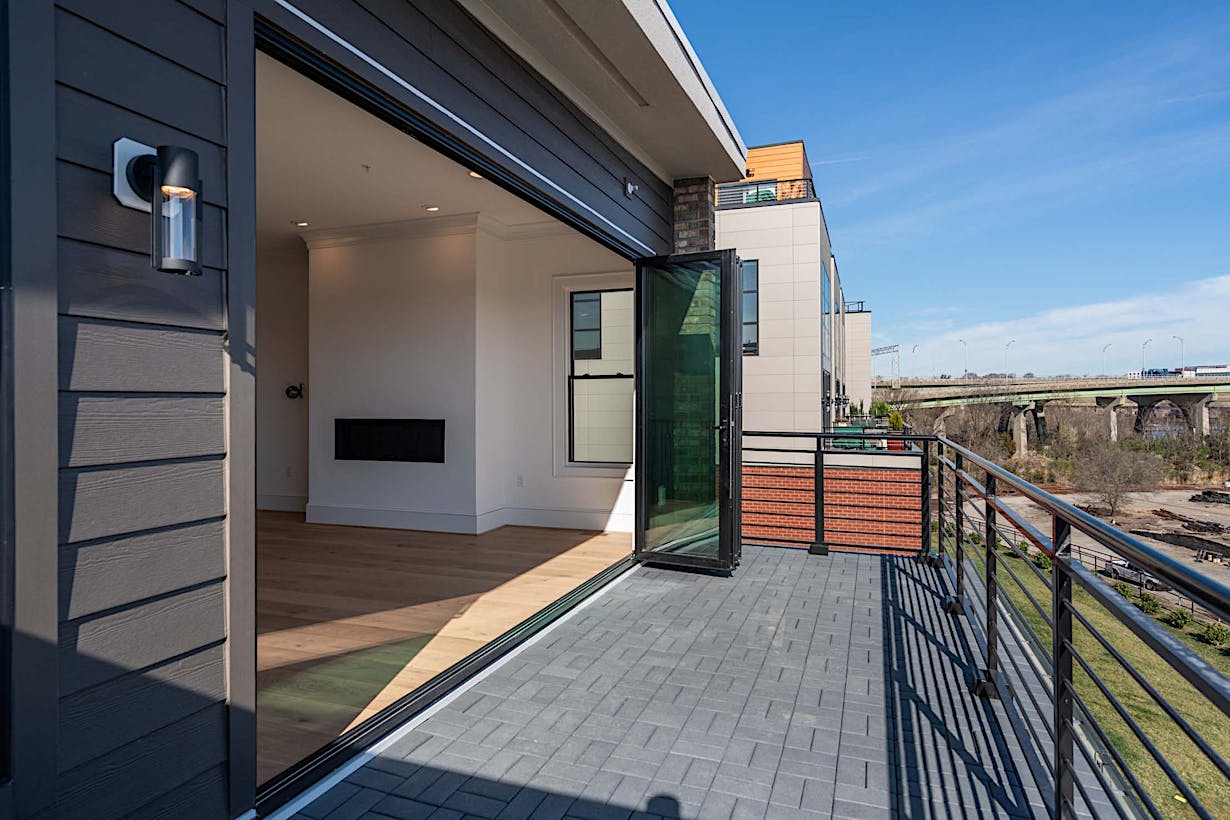 Modern folding deck doors lead from an empty room with wooden flooring to a spacious rooftop terrace.