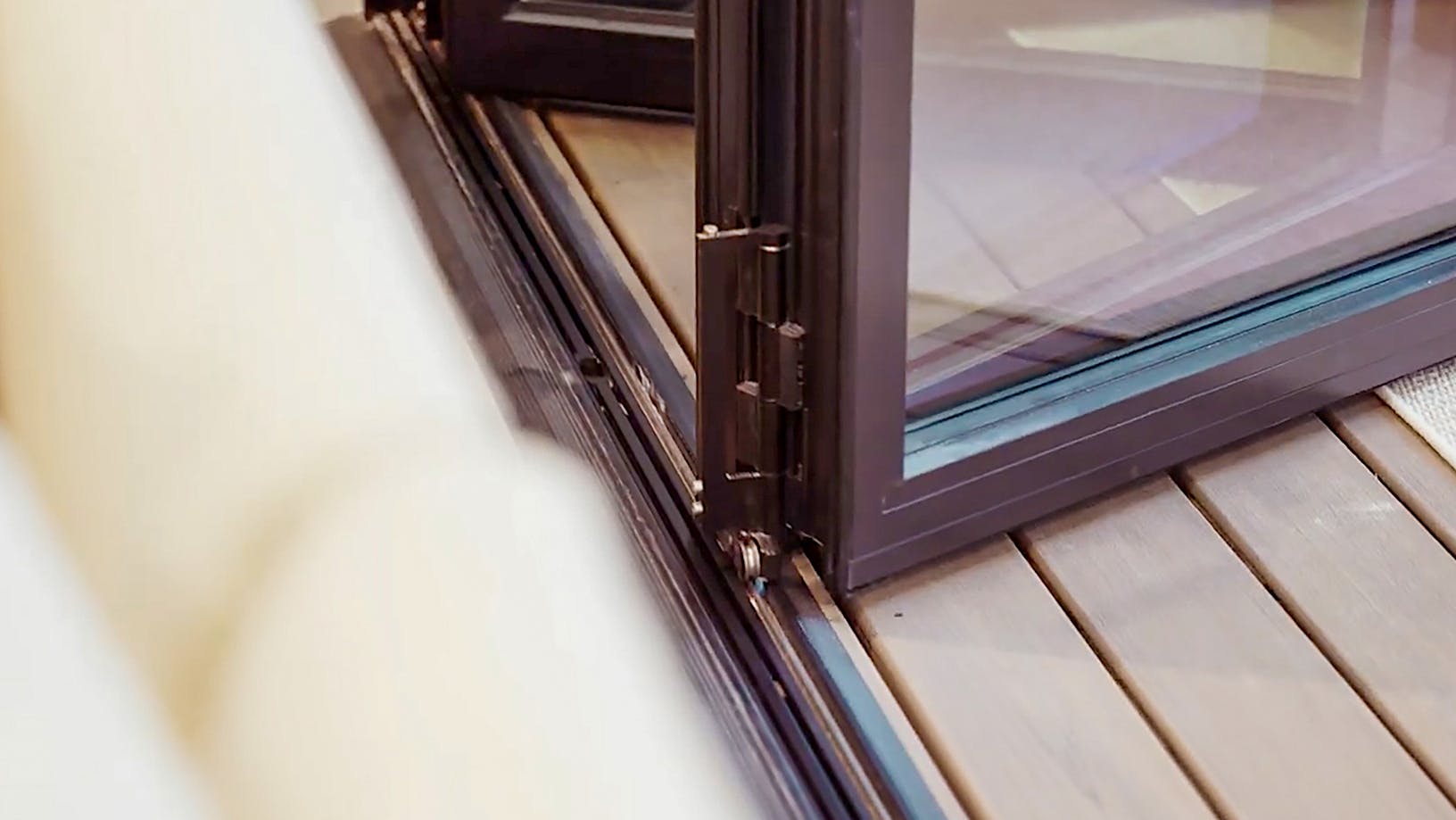 Close-up view of a partially open folding glass door with a black frame and floor track, placed above light-colored wooden flooring