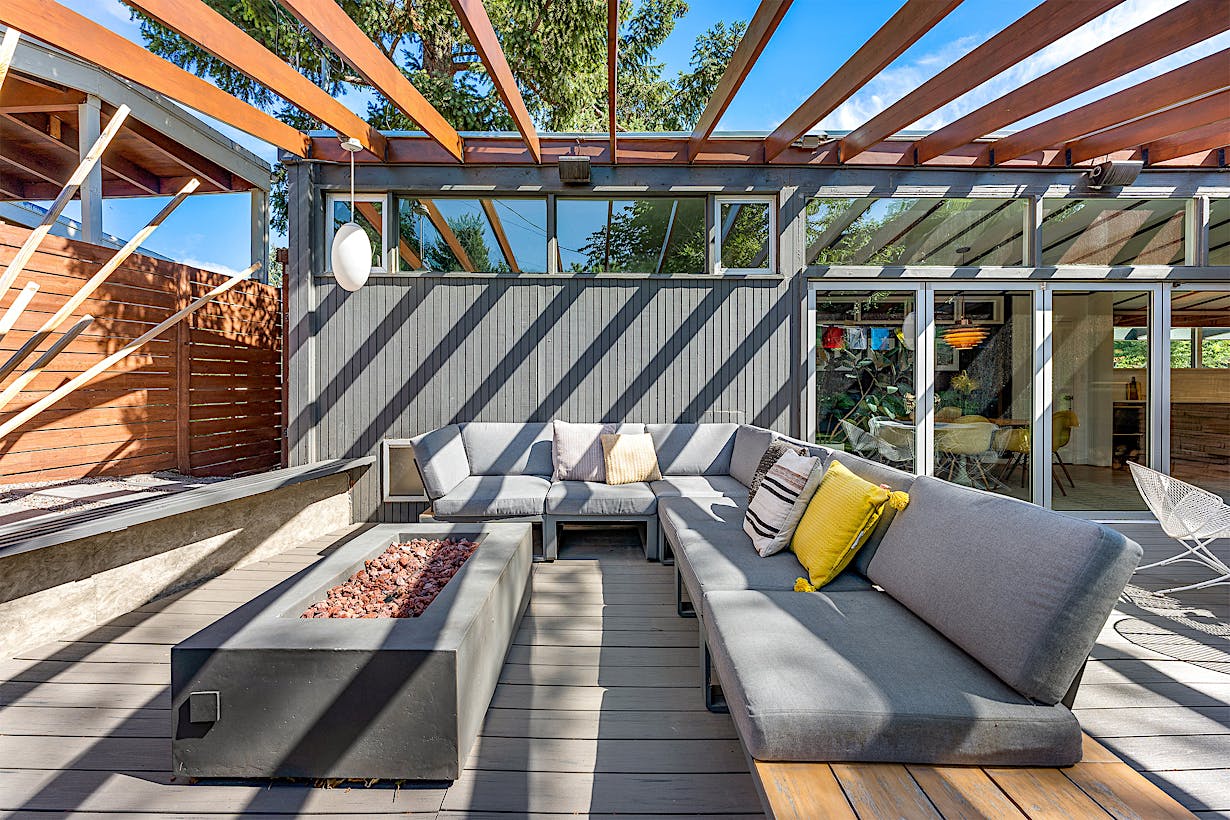 Modern outdoor patio with a sectional sofa around a rectangular fire pit table featuring folding glass doors leading to the interior.