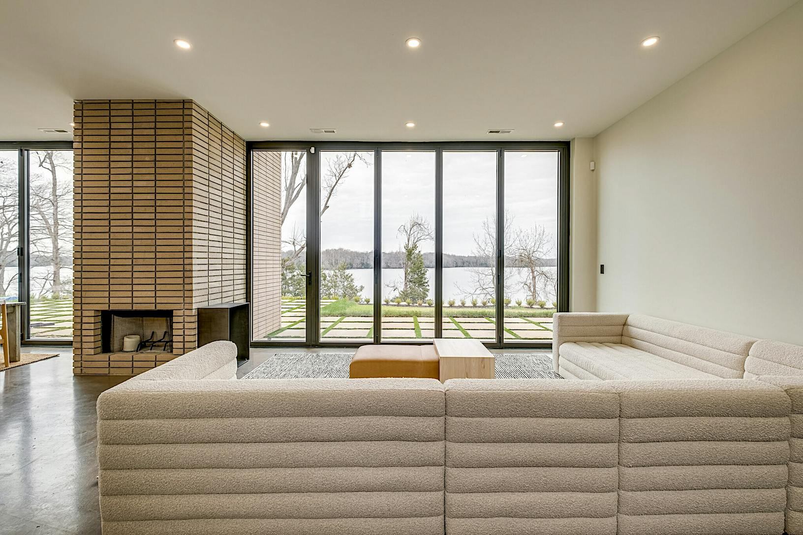Modern living room with large windows and glass wall panels providing a view of an outdoor landscape.
