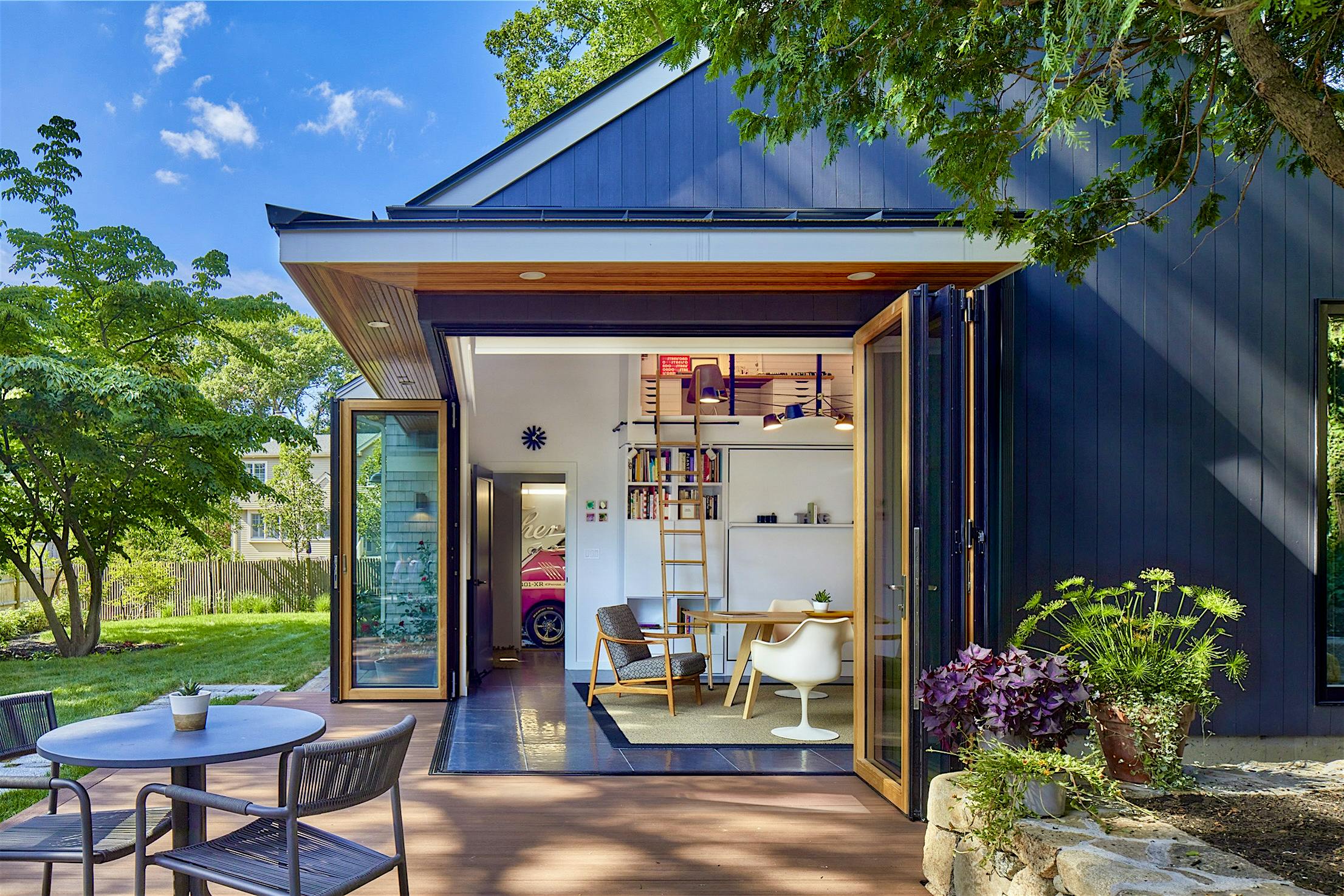 Modern house with grey exterior and folding glass patio doors revealing an interior with white walls and furniture.