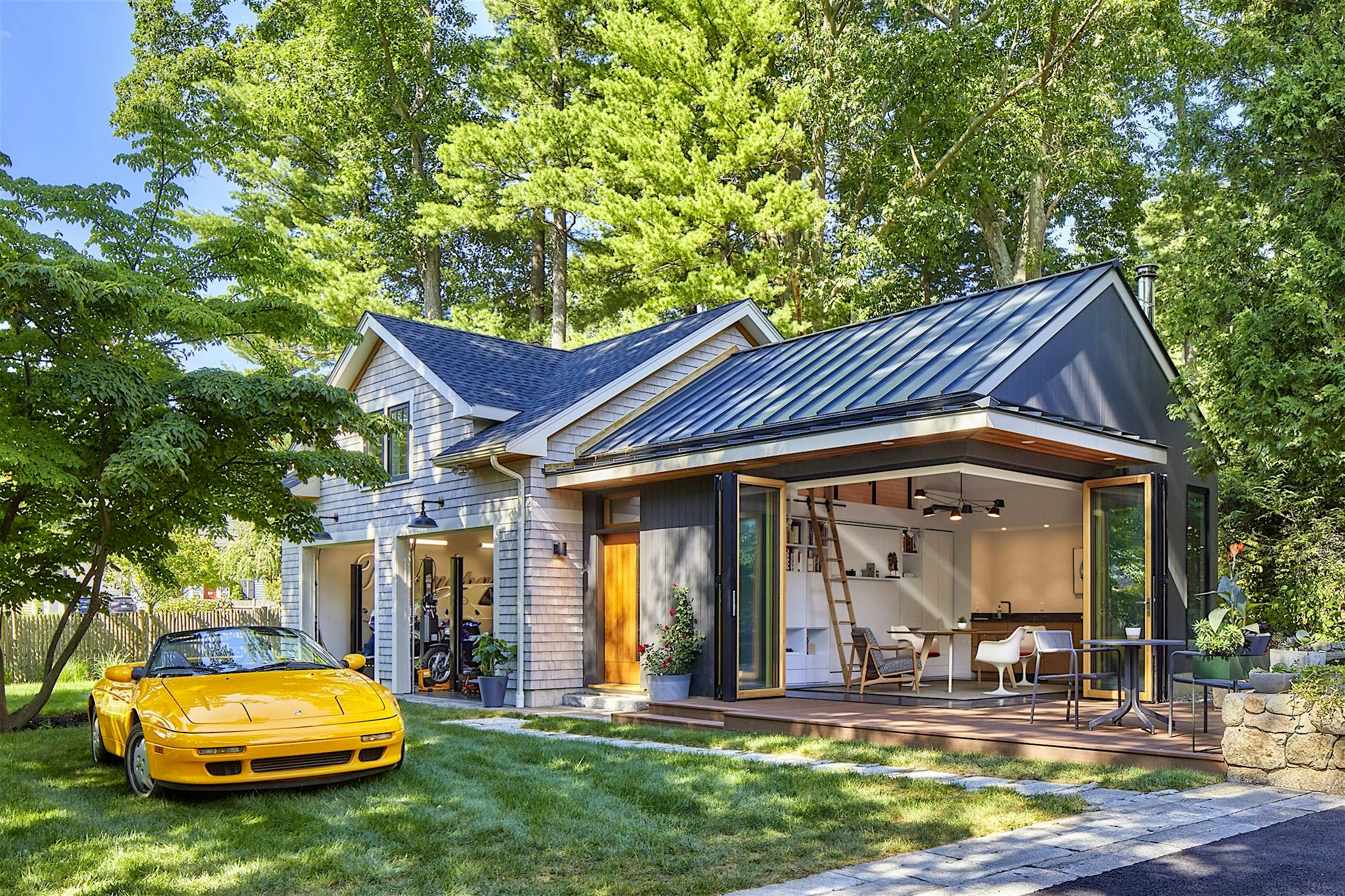 Cornerless bifolding doors lead to the backyard, while a yellow sports car is parked in the driveway.